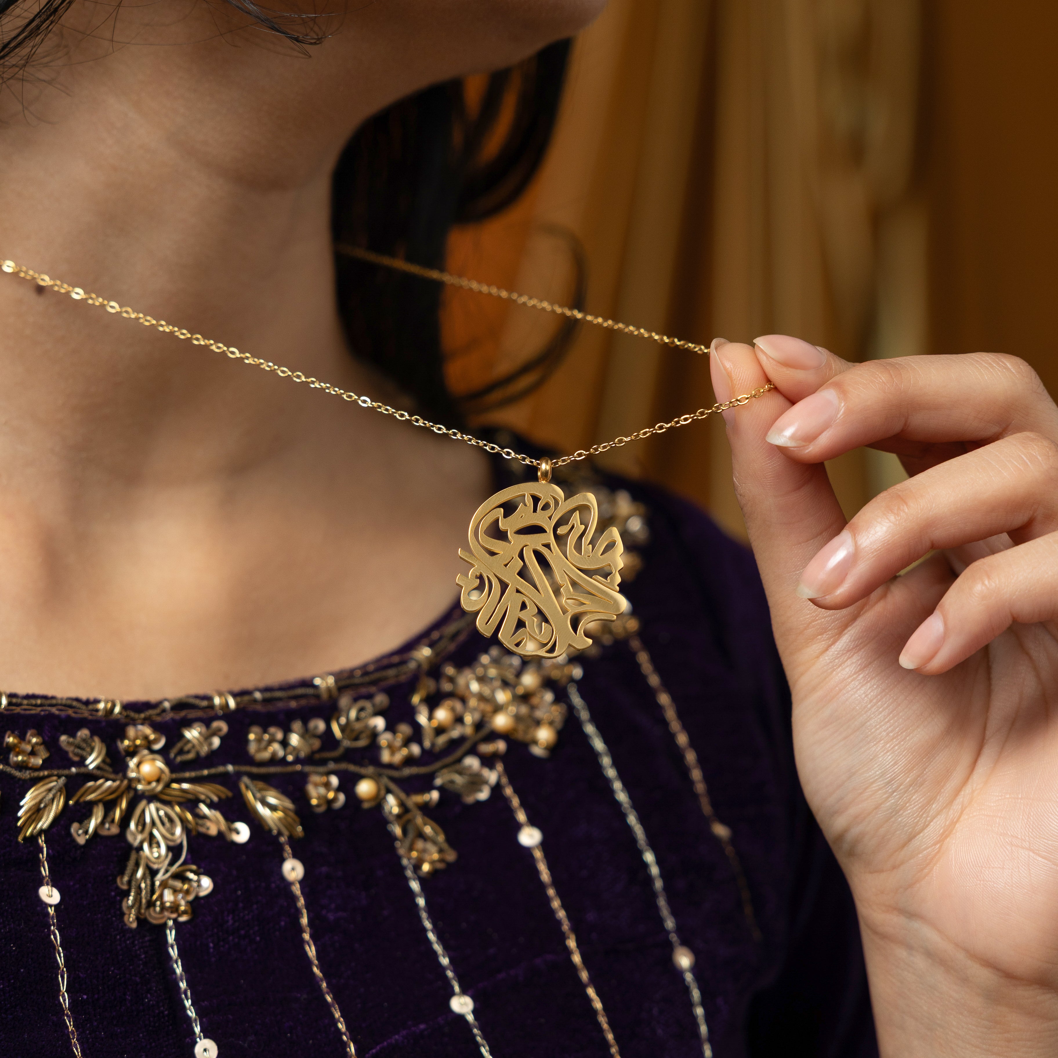 Close-up of the gold necklace, highlighting the delicate details of the calligraphy and the quality of the gold plating.