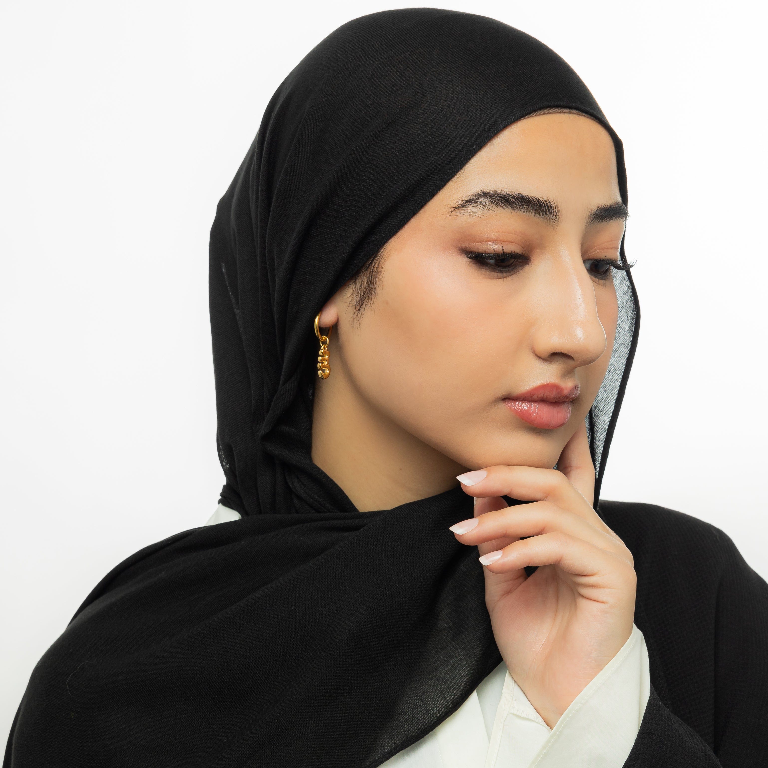 Close-up of gold bubble letter earrings featuring Arabic initials, shown against velvet pouch