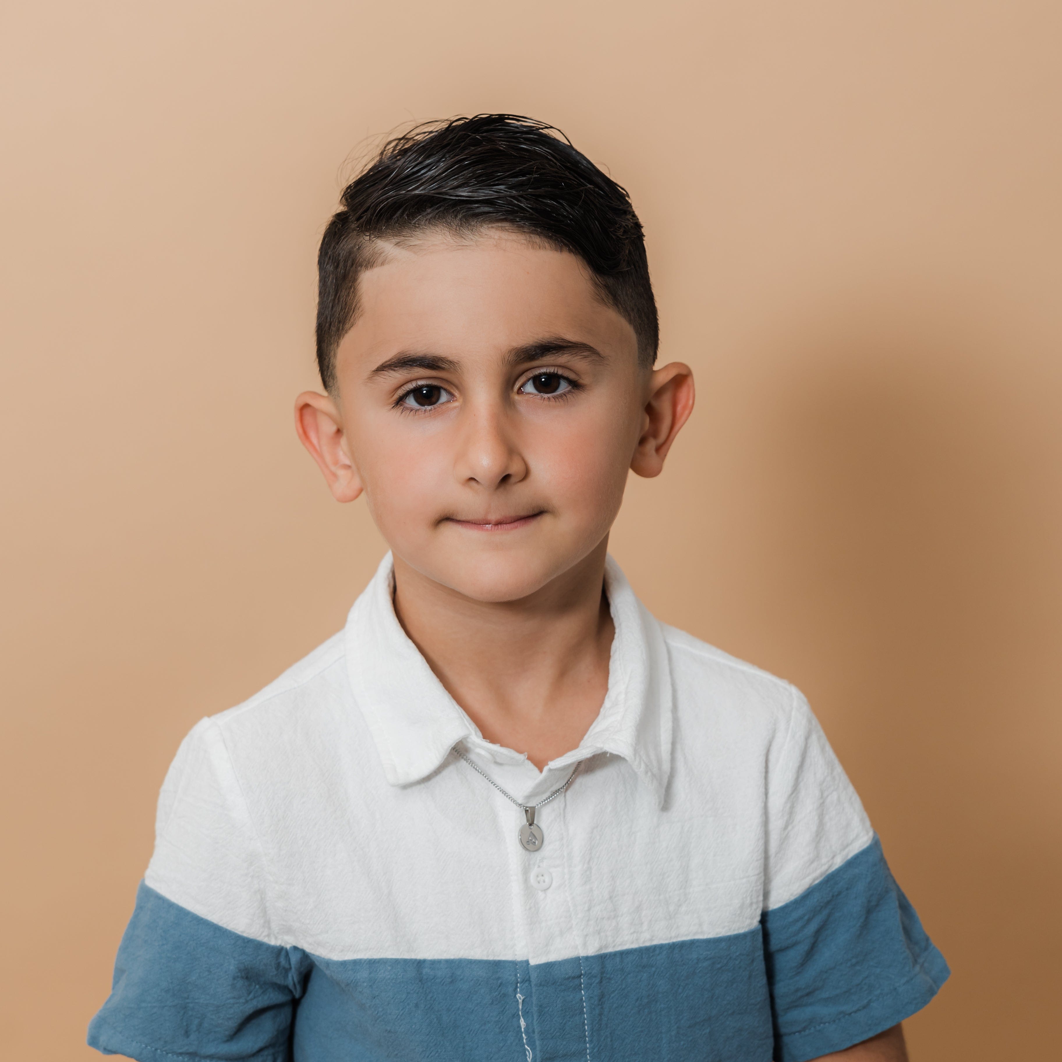 Young boy wearing the trendy letter necklace, showcasing how it complements his outfit.