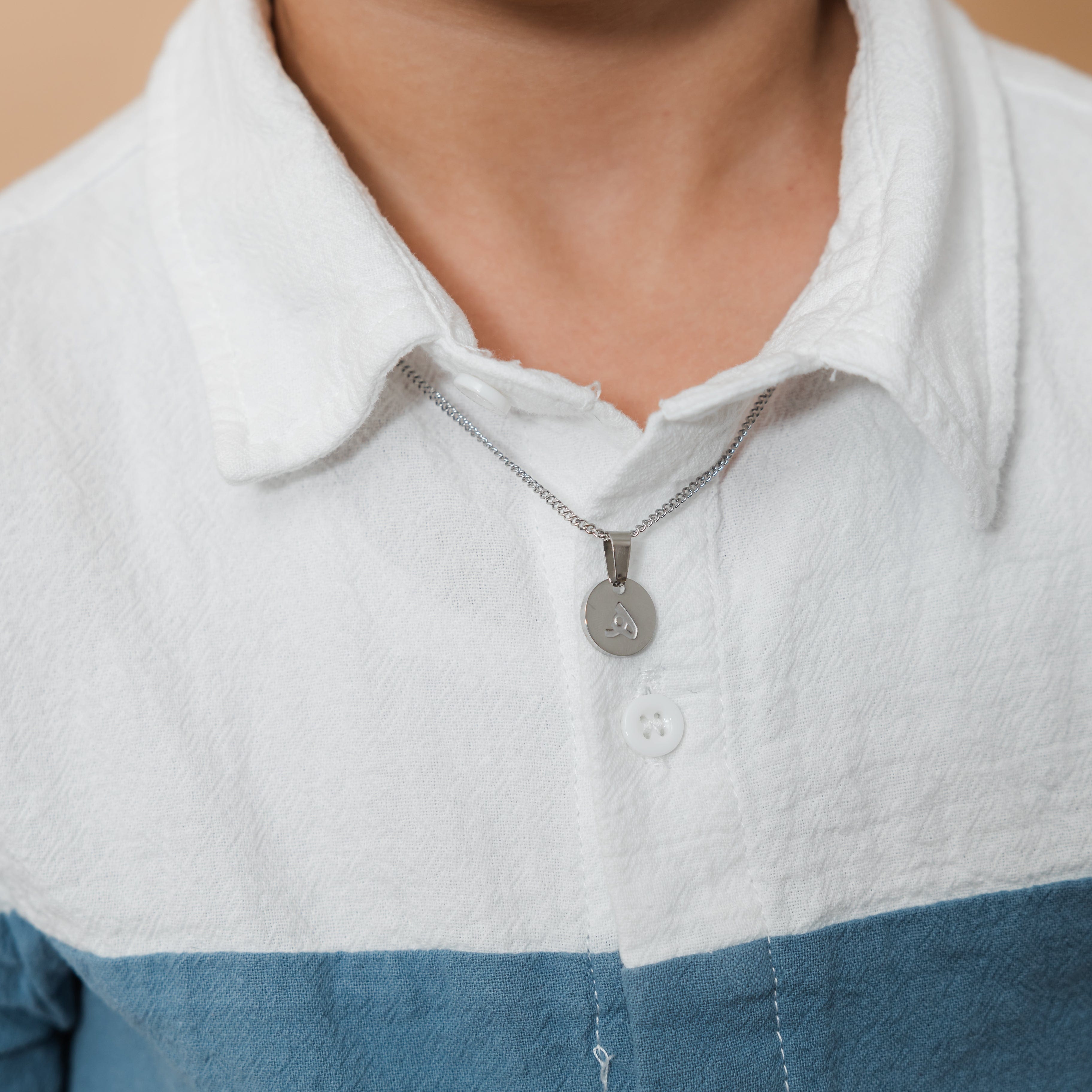 Young boy wearing the trendy letter necklace, showcasing how it complements his outfit.