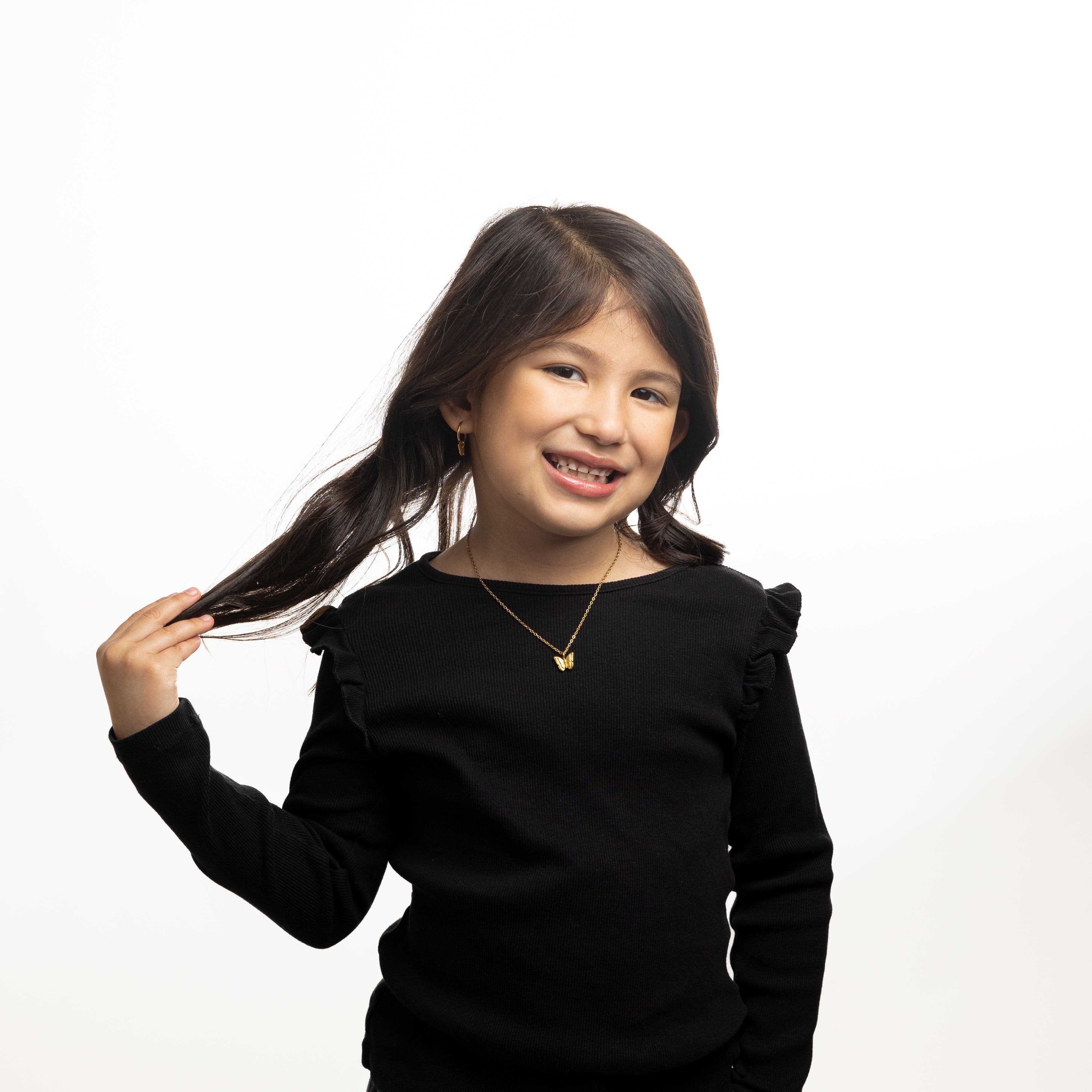 A little girl wearing the butterfly necklace with a bright smile, perfect for any outfit.