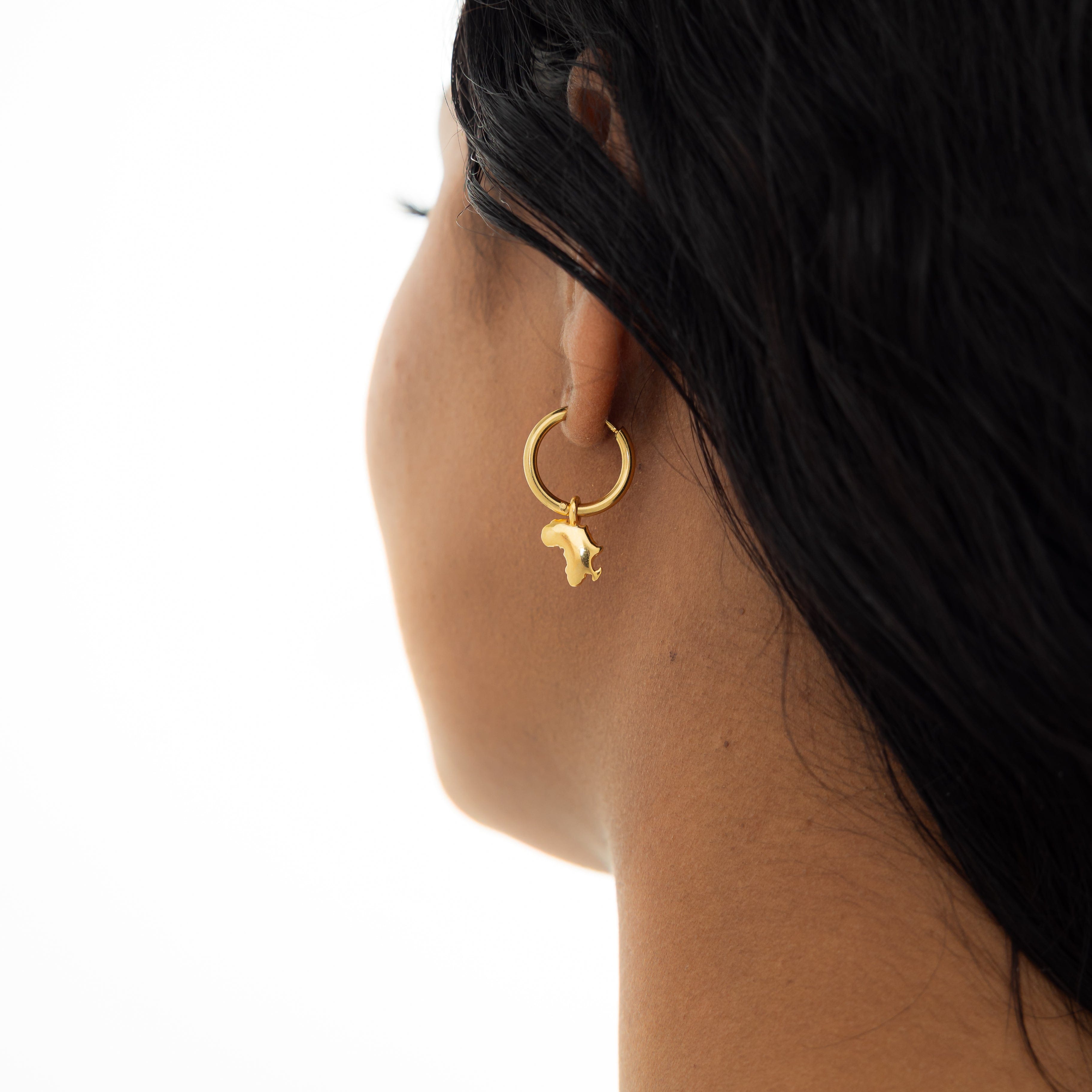 Model wearing personalized country map gold hoops at a casual outdoor event.