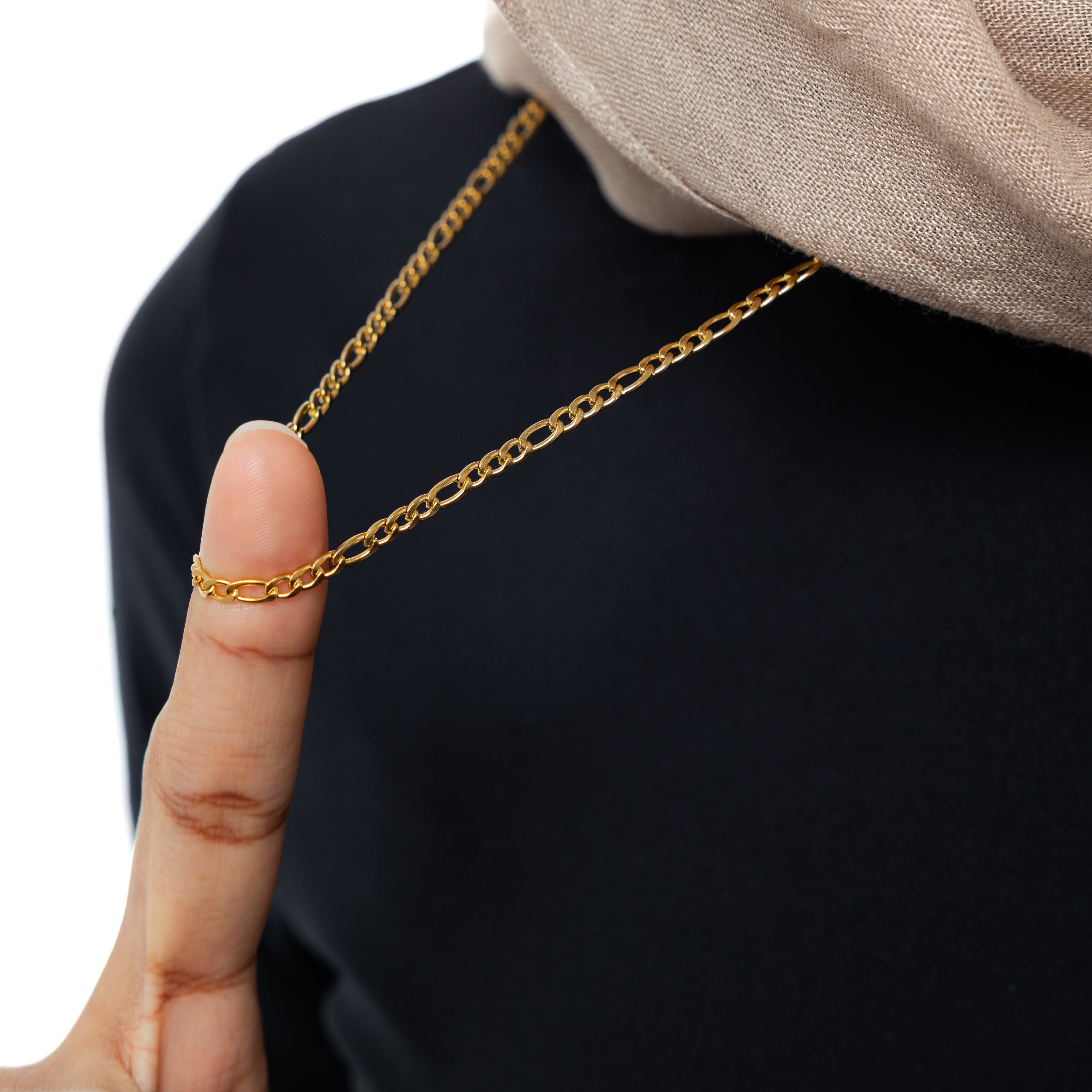 Close-up of the adjustable Figaro chain necklace highlighting its 18 karat gold finish.