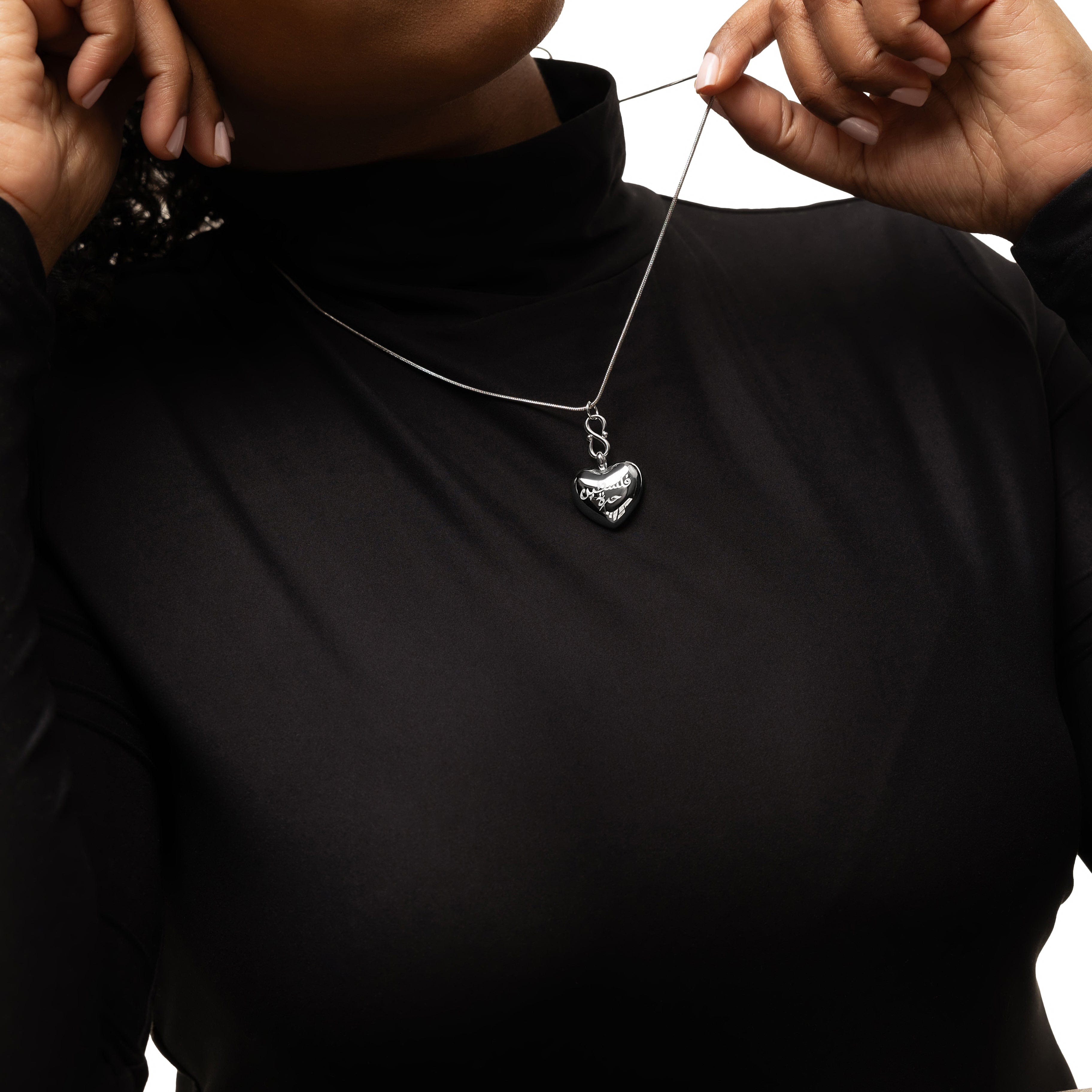 Close-up of the Free Palestine heart pendant, highlighting the engraved Arabic text.