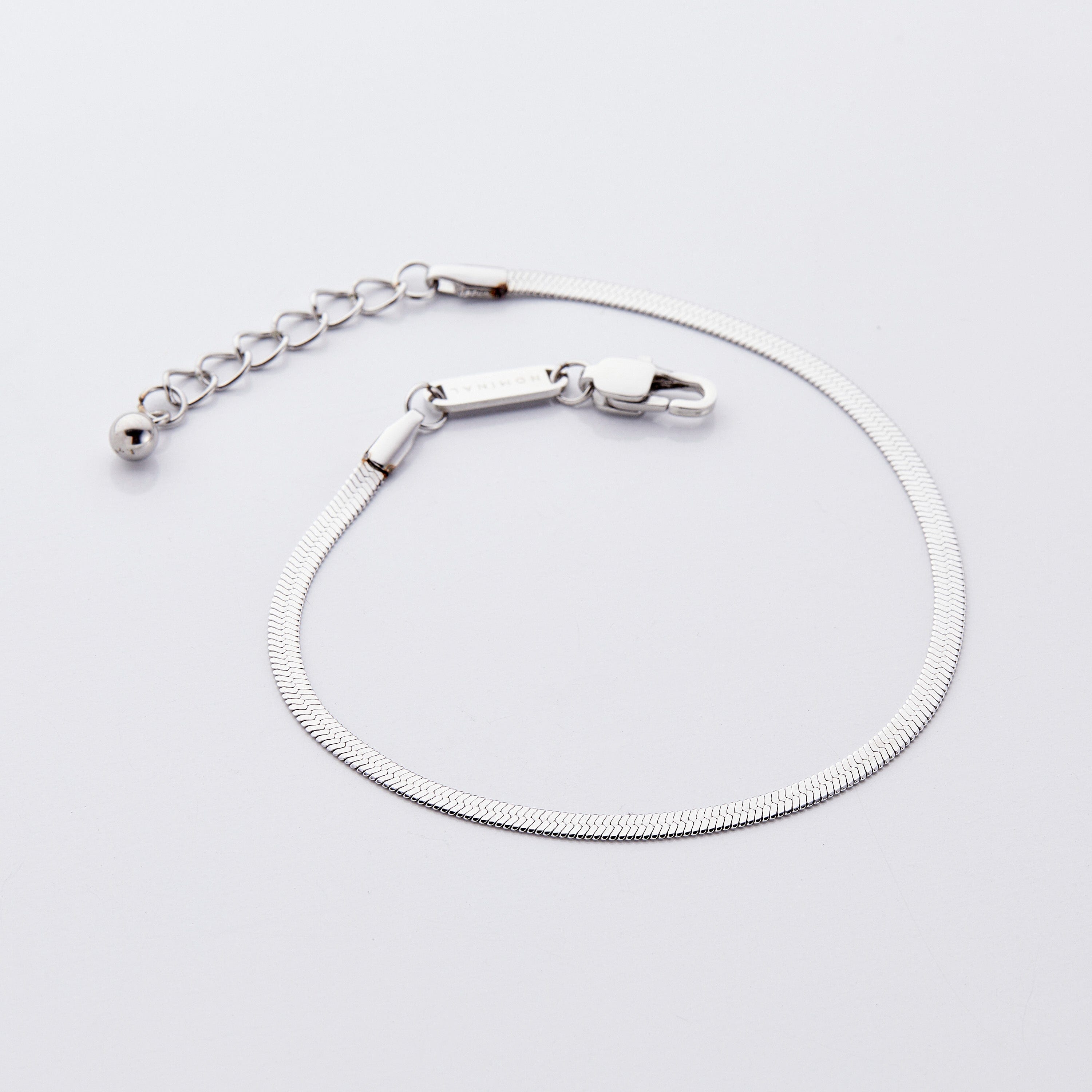 The Liquid Gold Herringbone Chain Anklet displayed in a velvet pouch, emphasizing its luxurious feel.