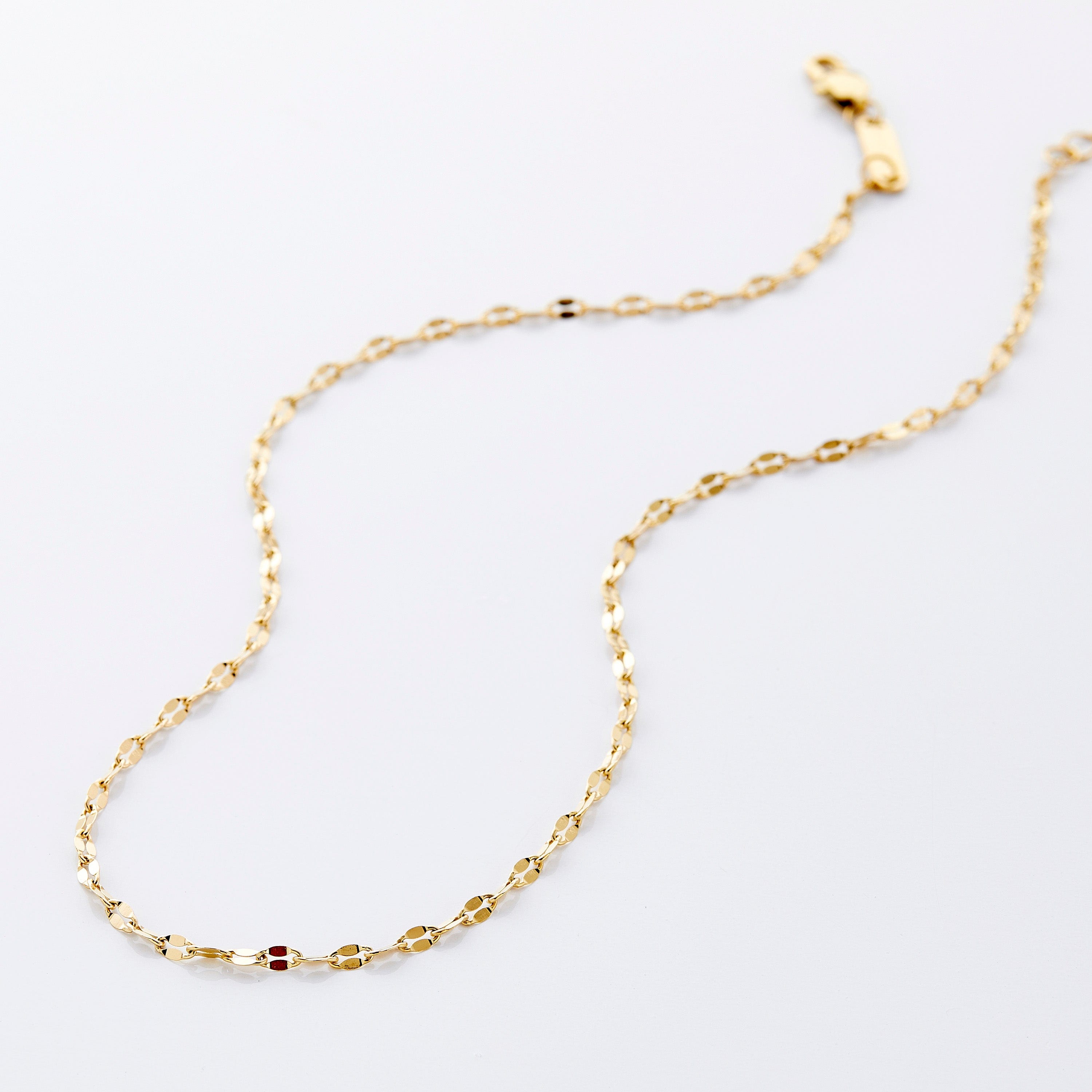 Gold flutter chain necklace displayed on a soft velvet background.