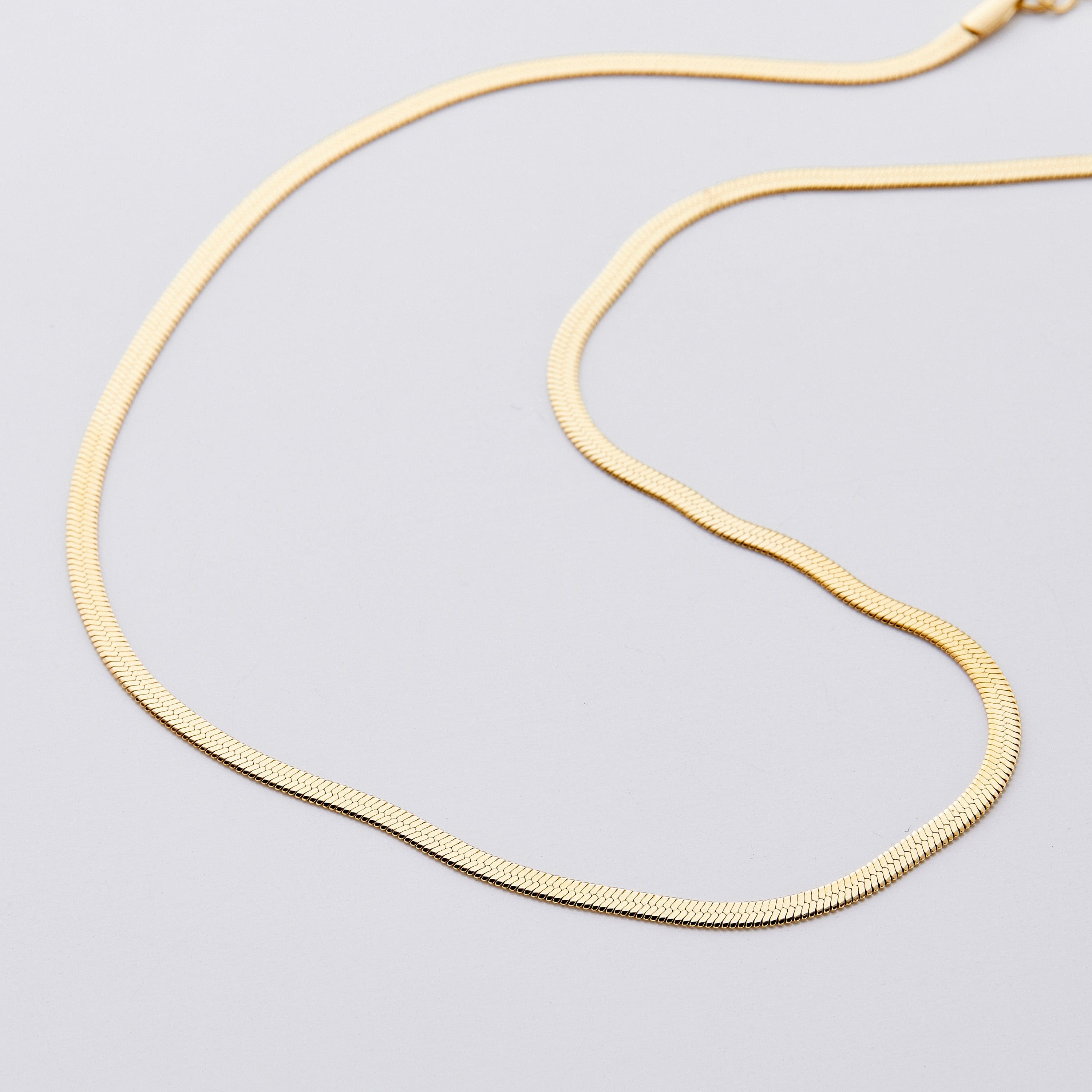 Close-up of the Liquid Gold Herringbone Necklace highlighting its shiny finish and unique pattern.