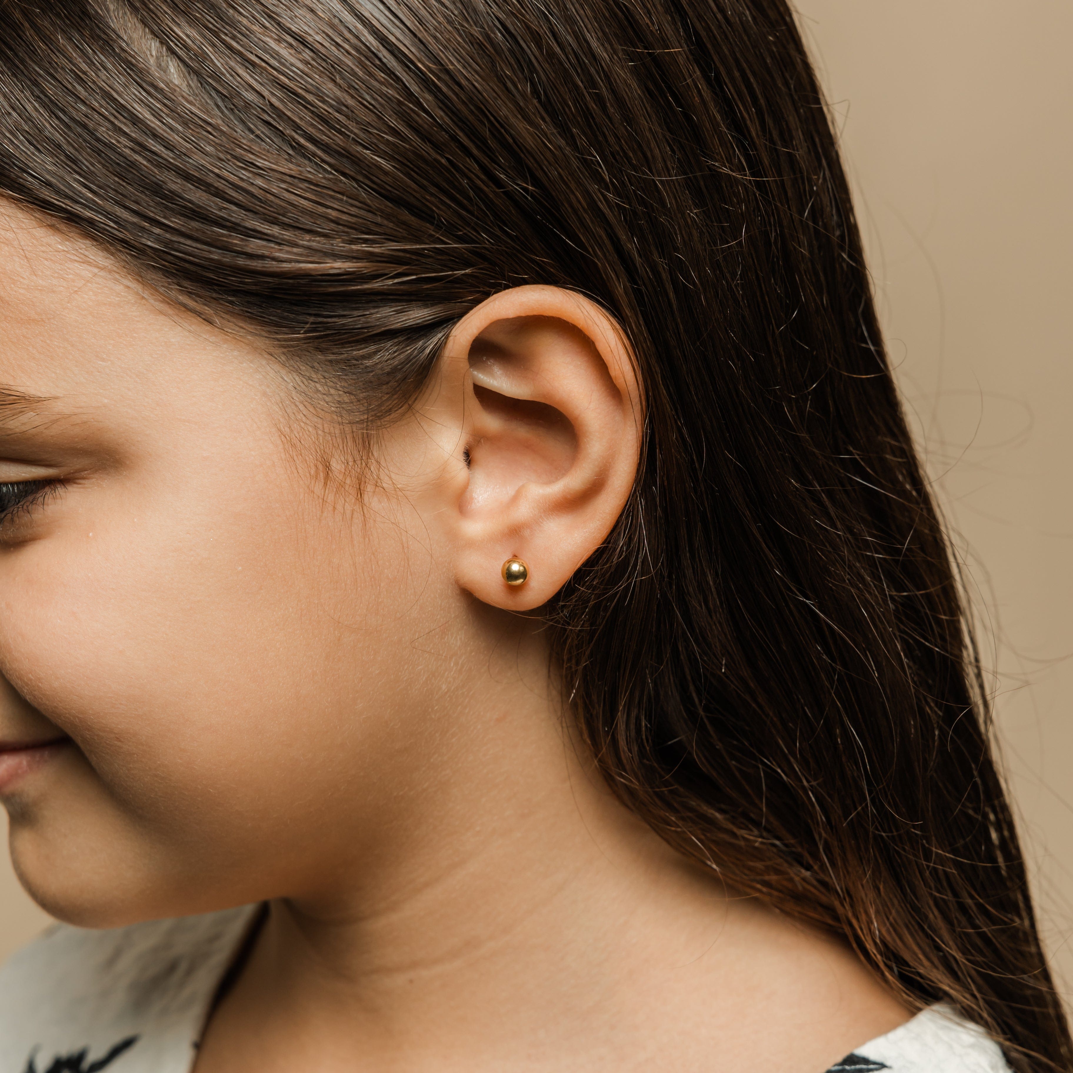 Close-up of real gold stud earrings for children, focusing on the ball-screw backing for added safety.