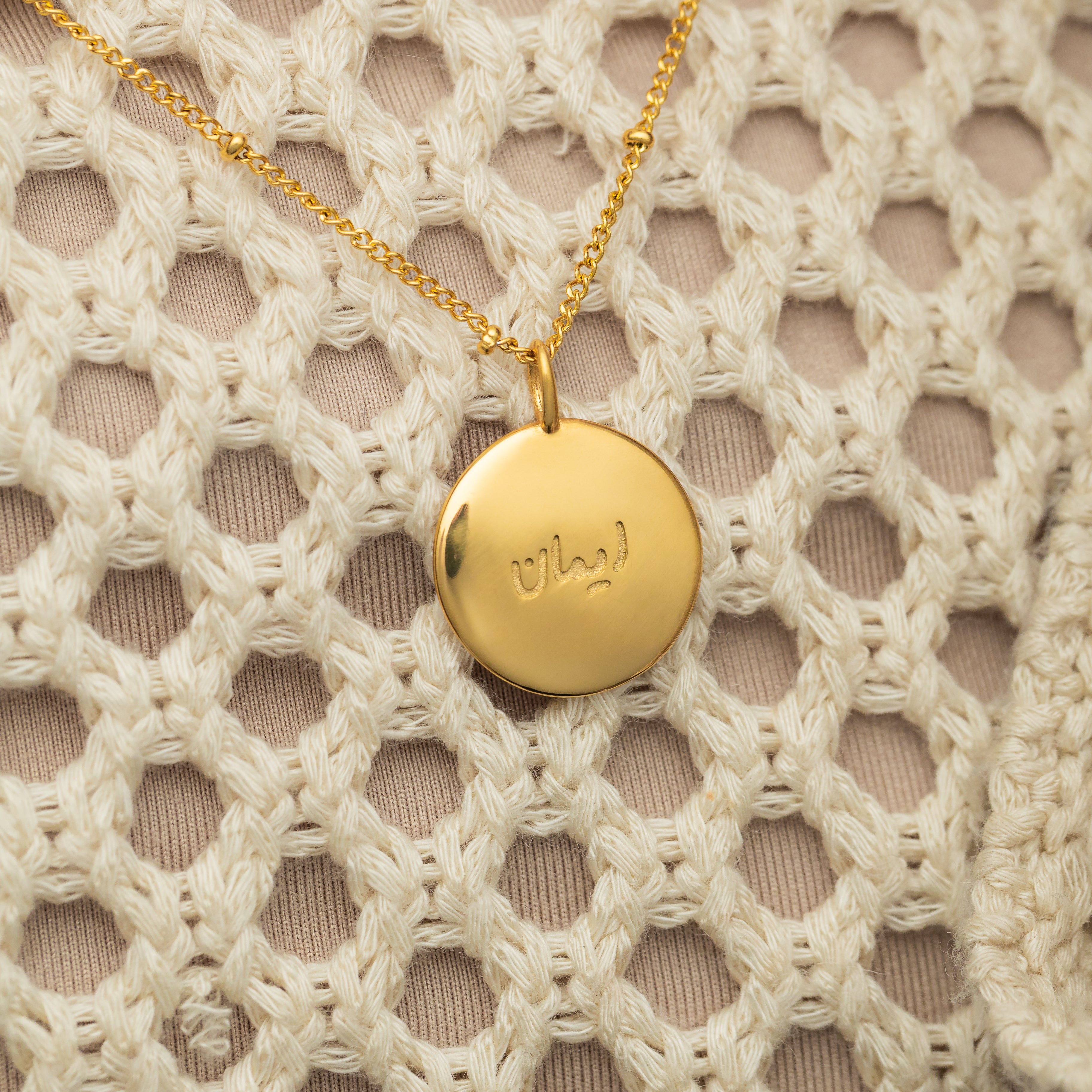 Close-up of the Iman Faith Charm highlighting its Arabic engraving and gold finish.
