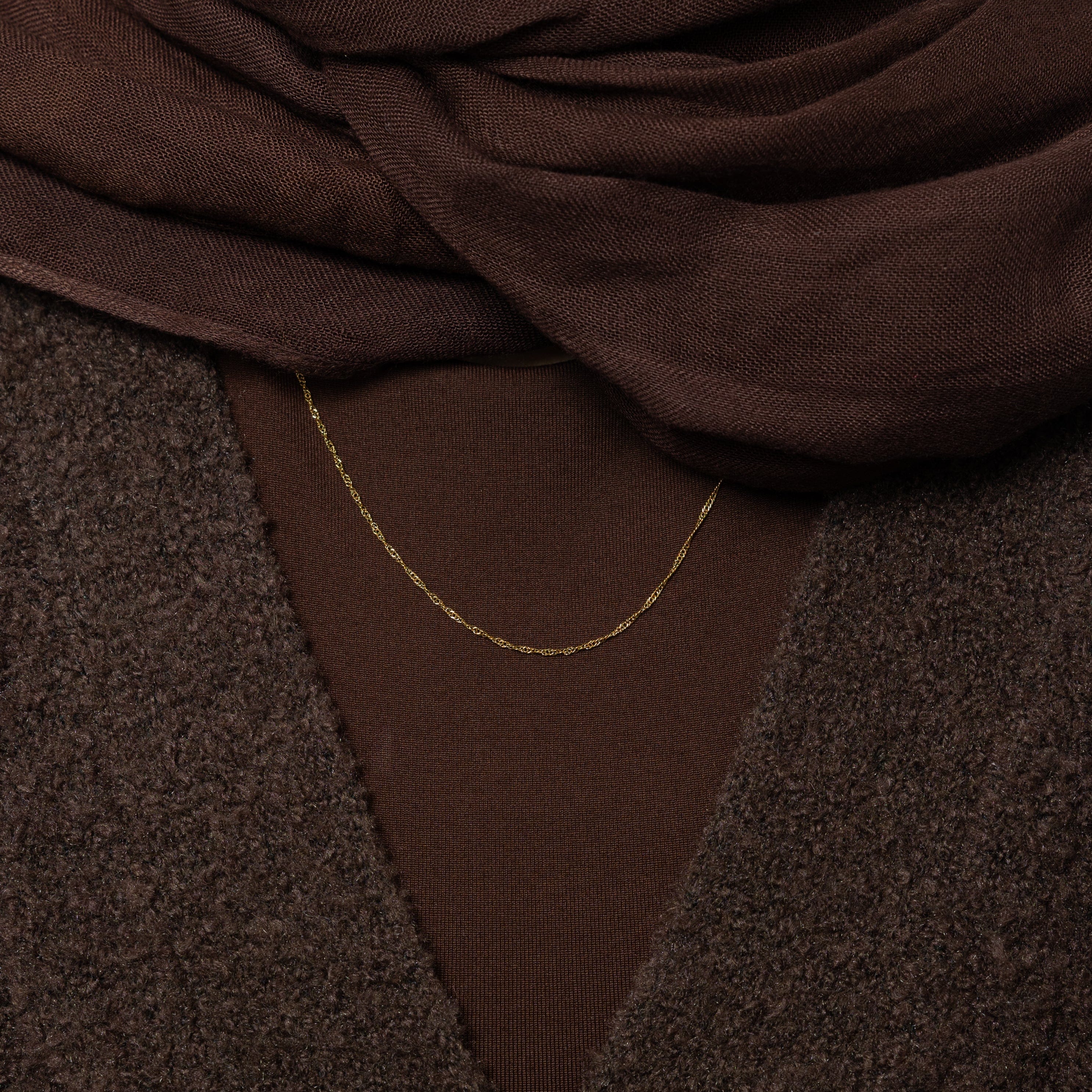 The gold twisted chain necklace styled with casual and formal outfits, illustrating its versatility.