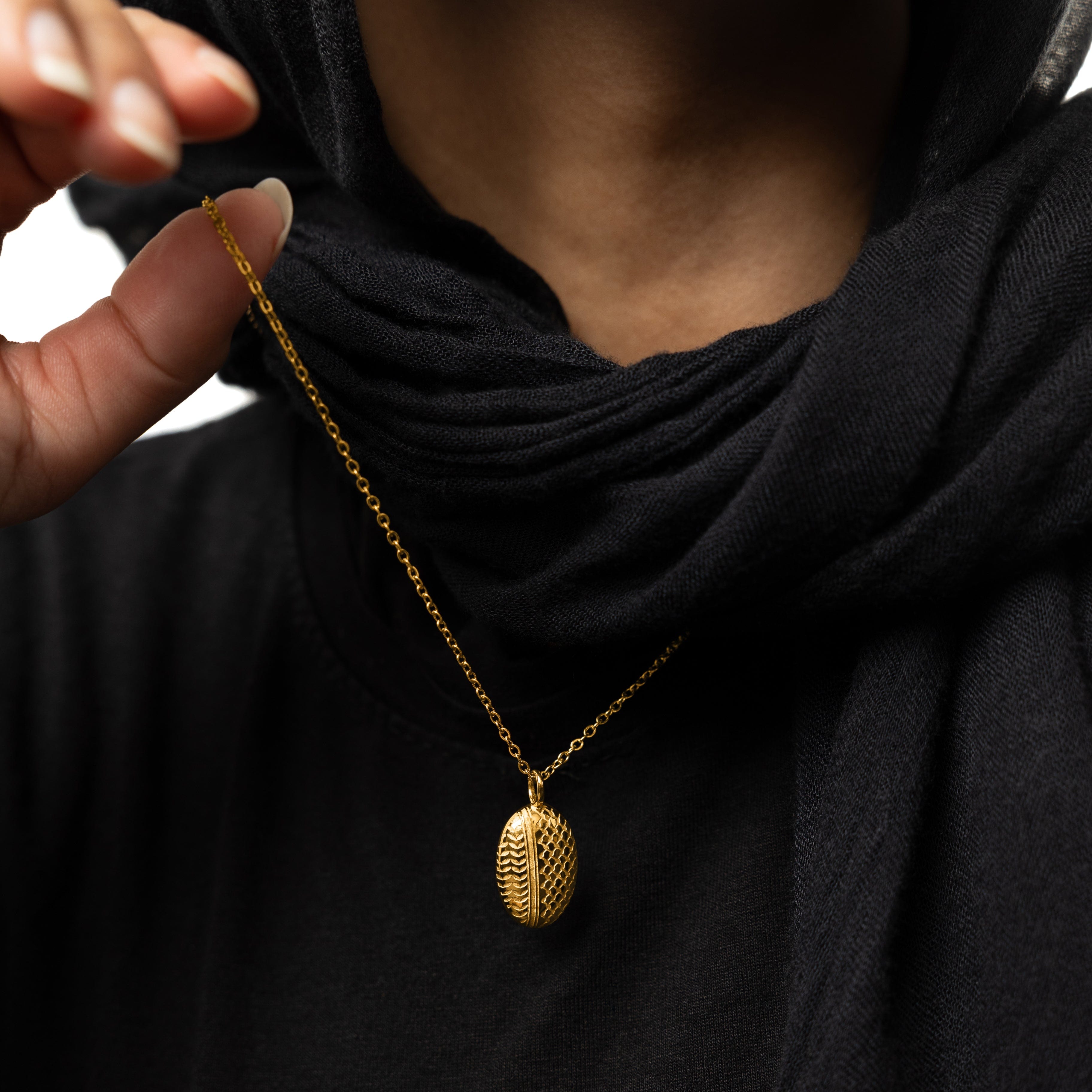 Close-up of gold-plated keffiyeh necklace pendant highlighting olive leaf motif