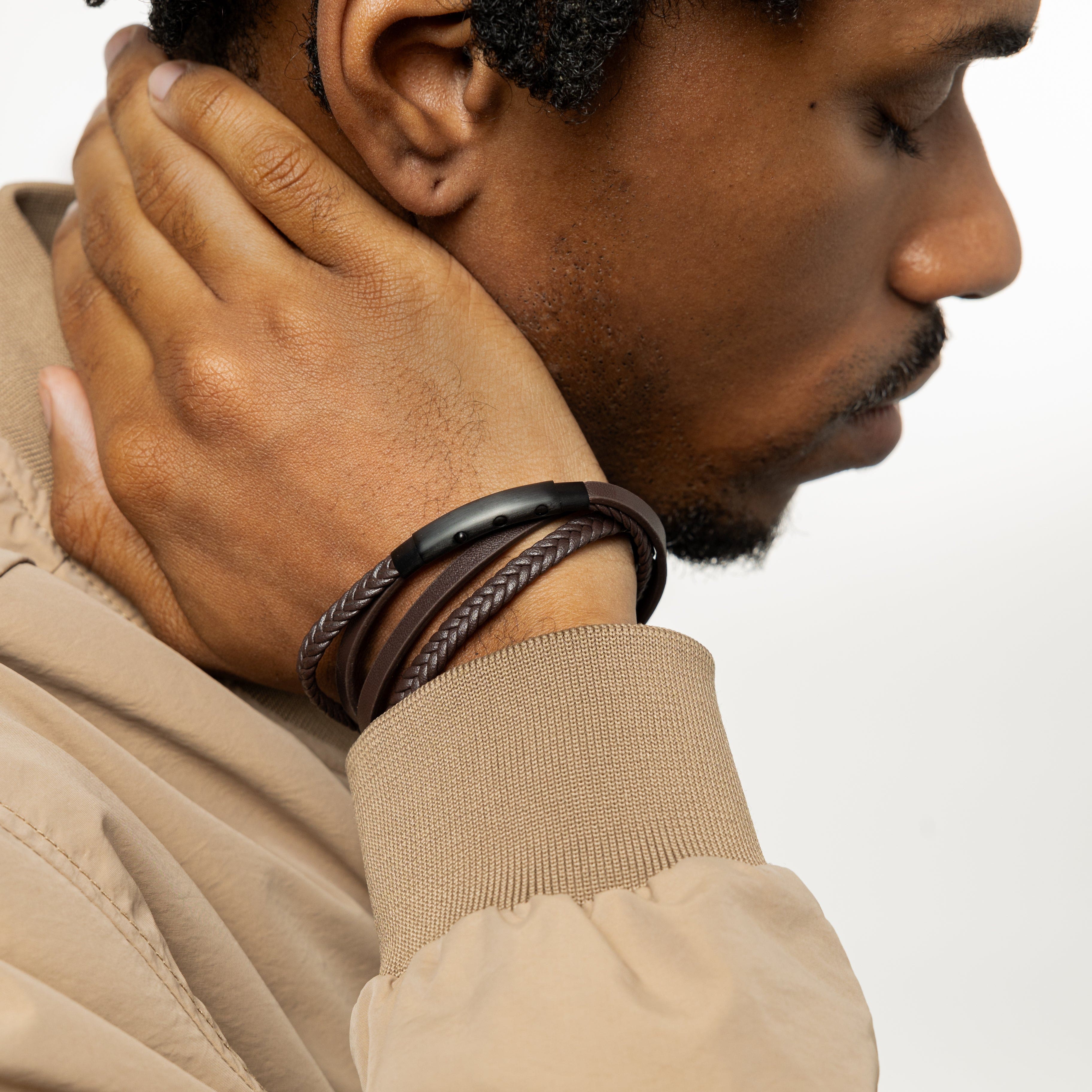 Styled shot of mens jewelry on wrist with black leather bracelet layered under sleeve