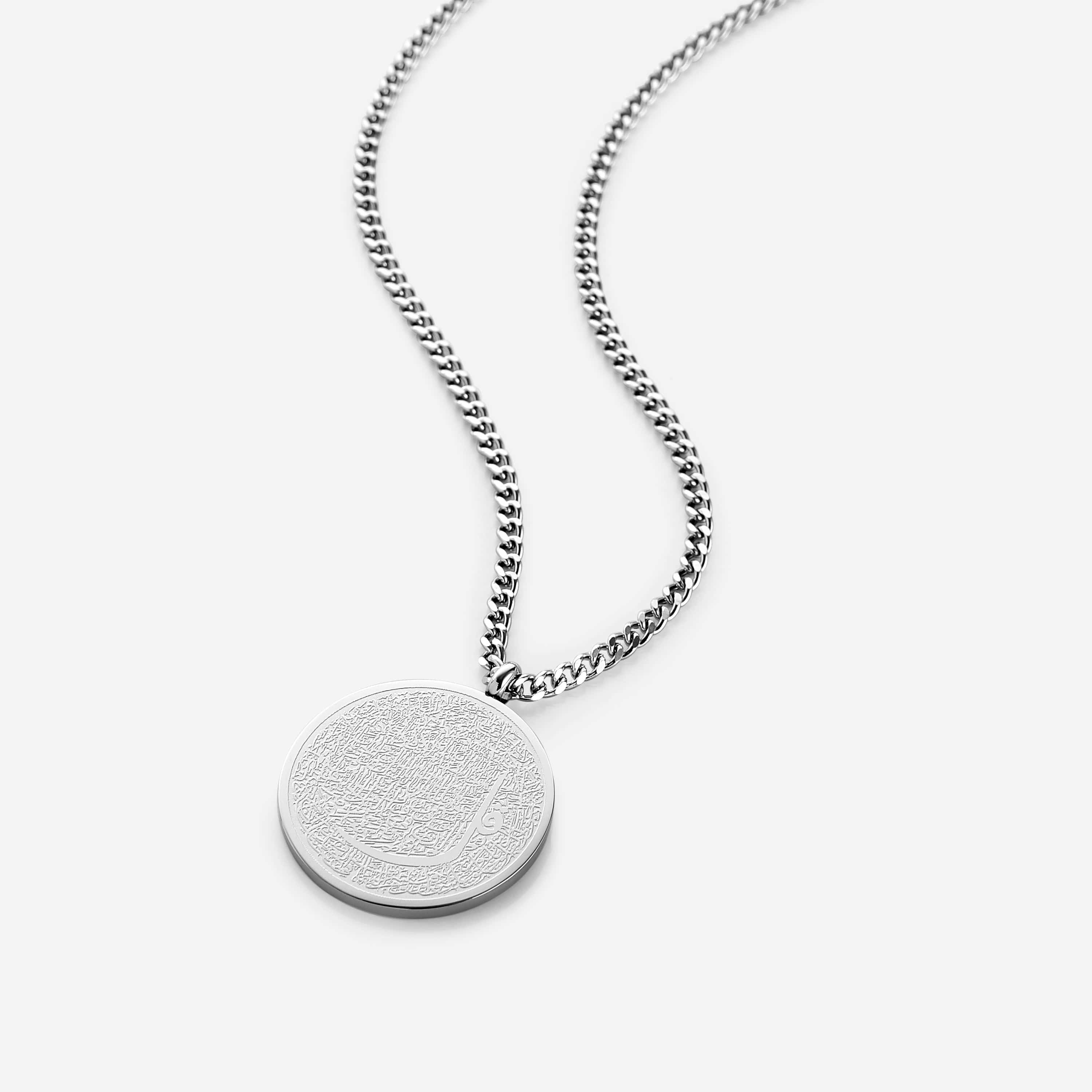 Elegant Qur'an verse token necklace displayed on a wooden background, showcasing intricate calligraphy.