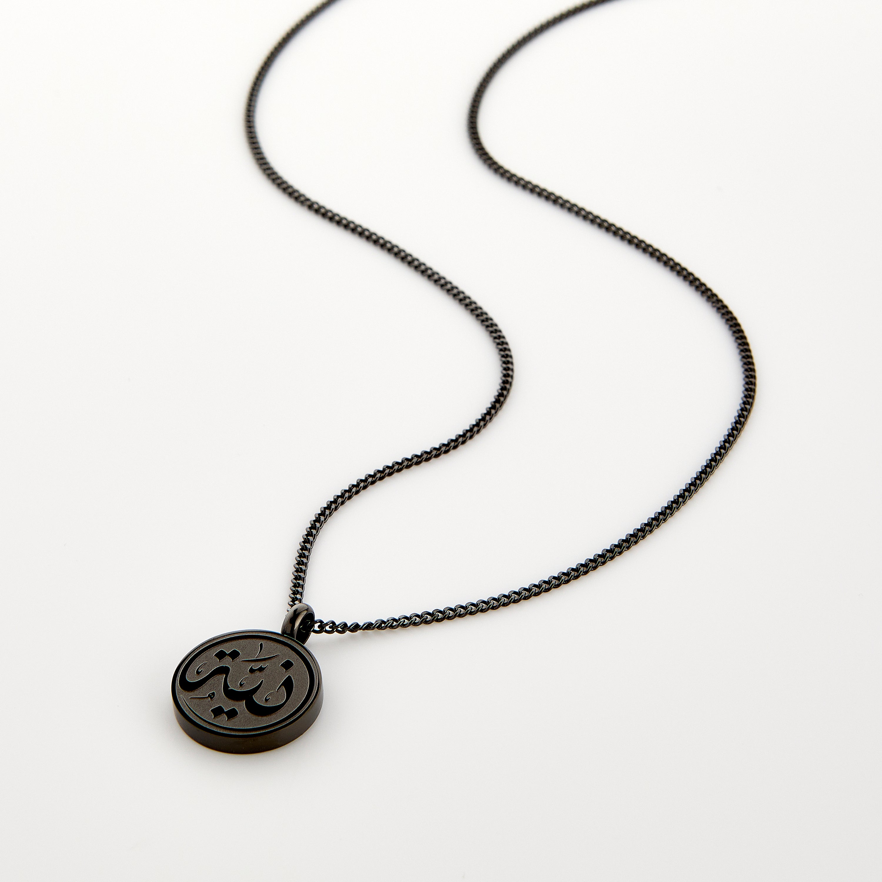 Close-up of mens necklace with Arabic Niyyah calligraphy pendant on velvet pouch