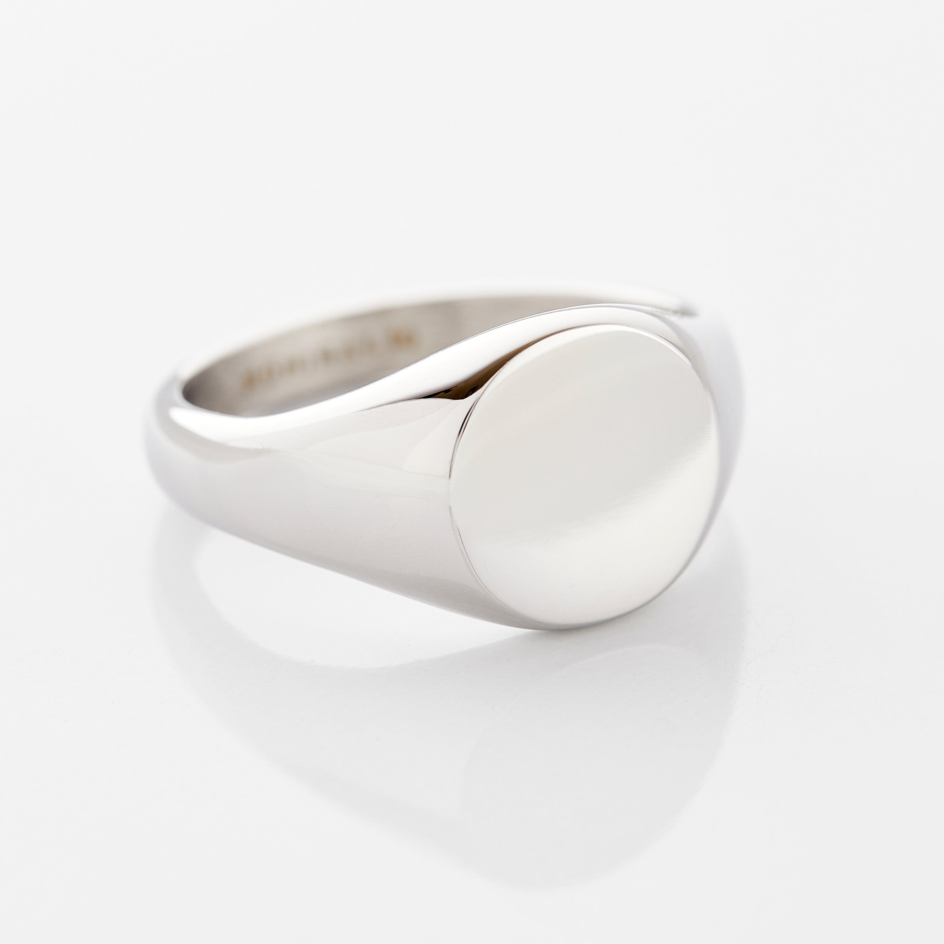 Classic round signet ring in stainless steel, displayed on a rustic wooden surface.