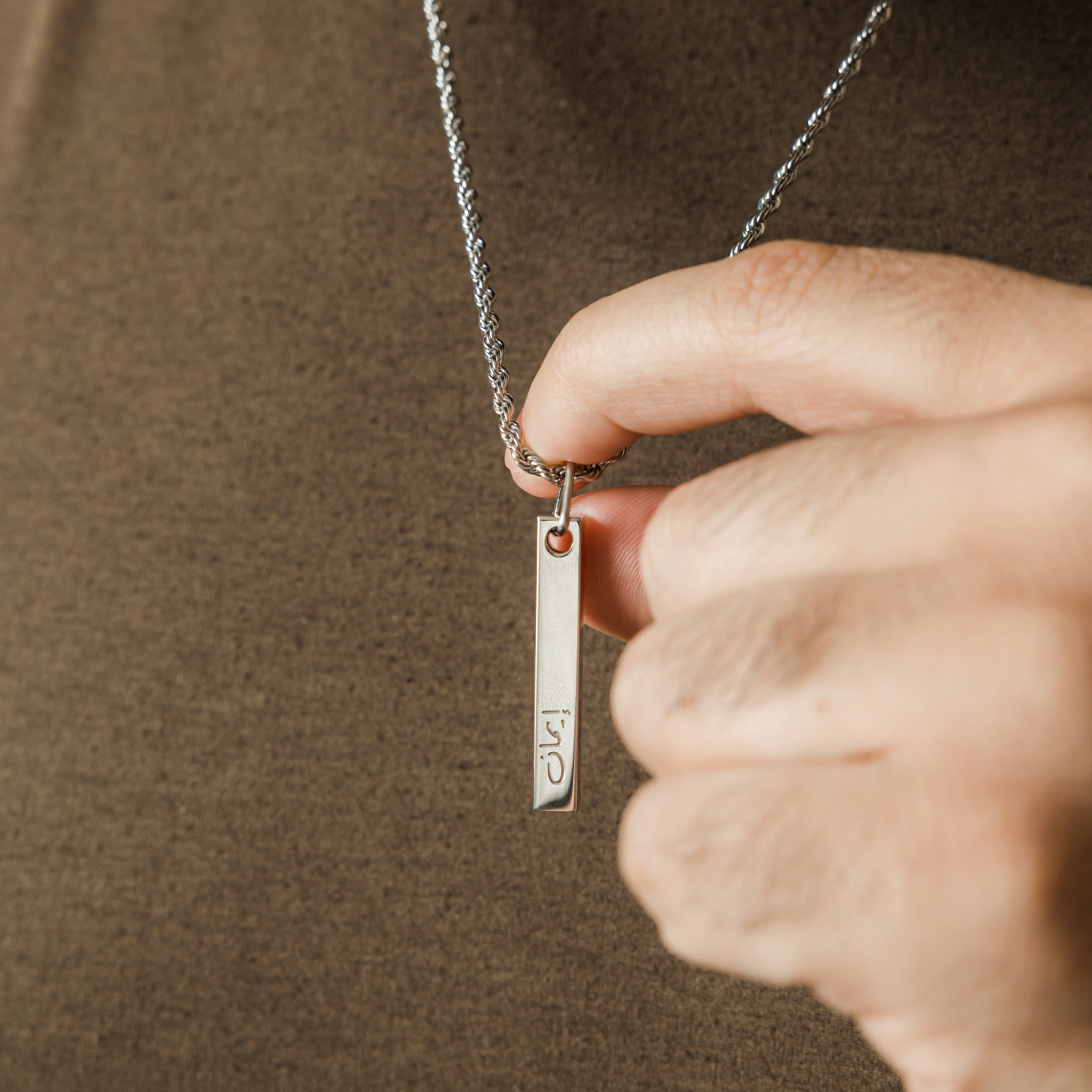 Close-up of the stainless steel pendant with faith engraved in Arabic.