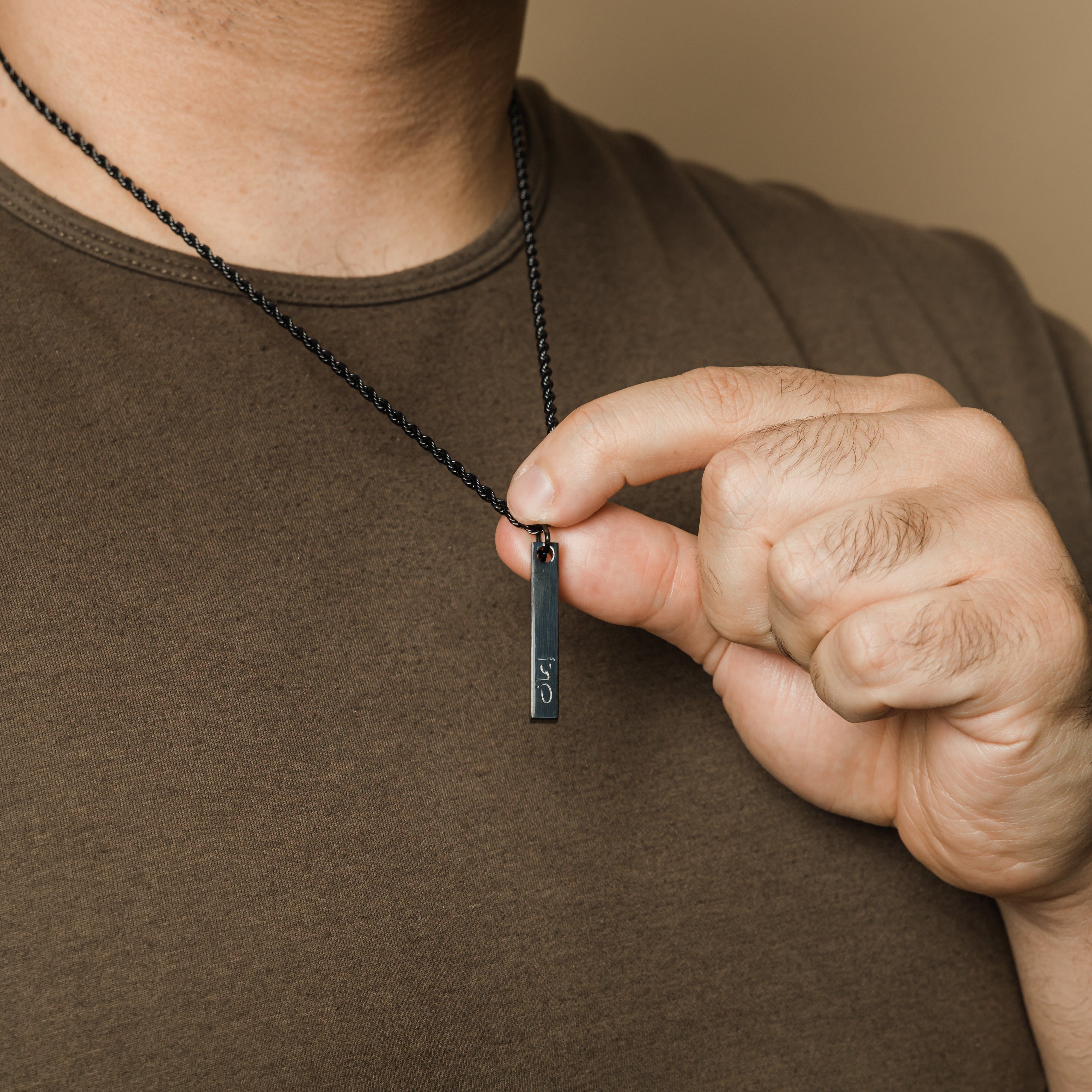 Engraved faith bar necklace for men displayed on a wooden table.