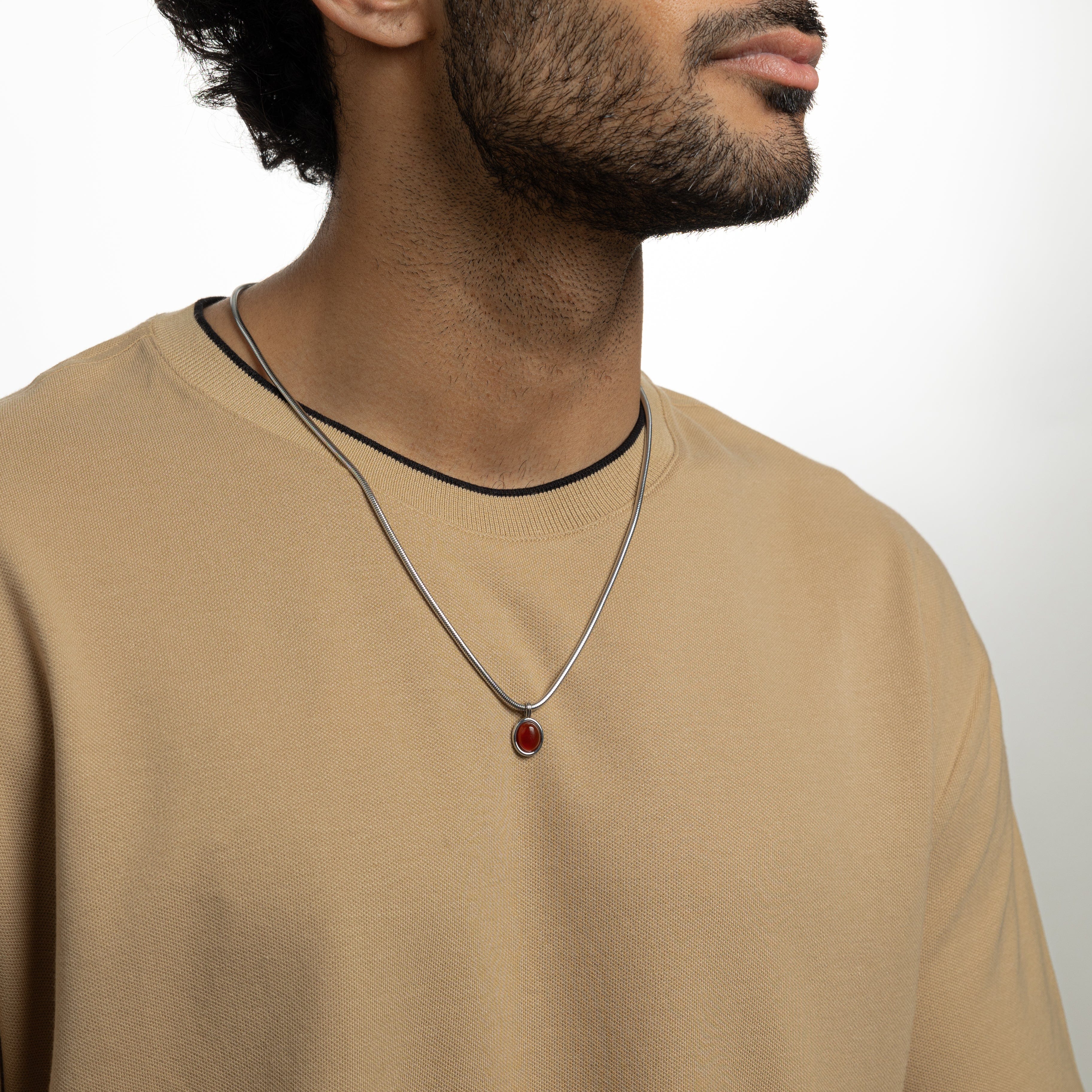 Mens red agate necklace displayed on a dark background, showcasing the steel pendant and harmony chain.