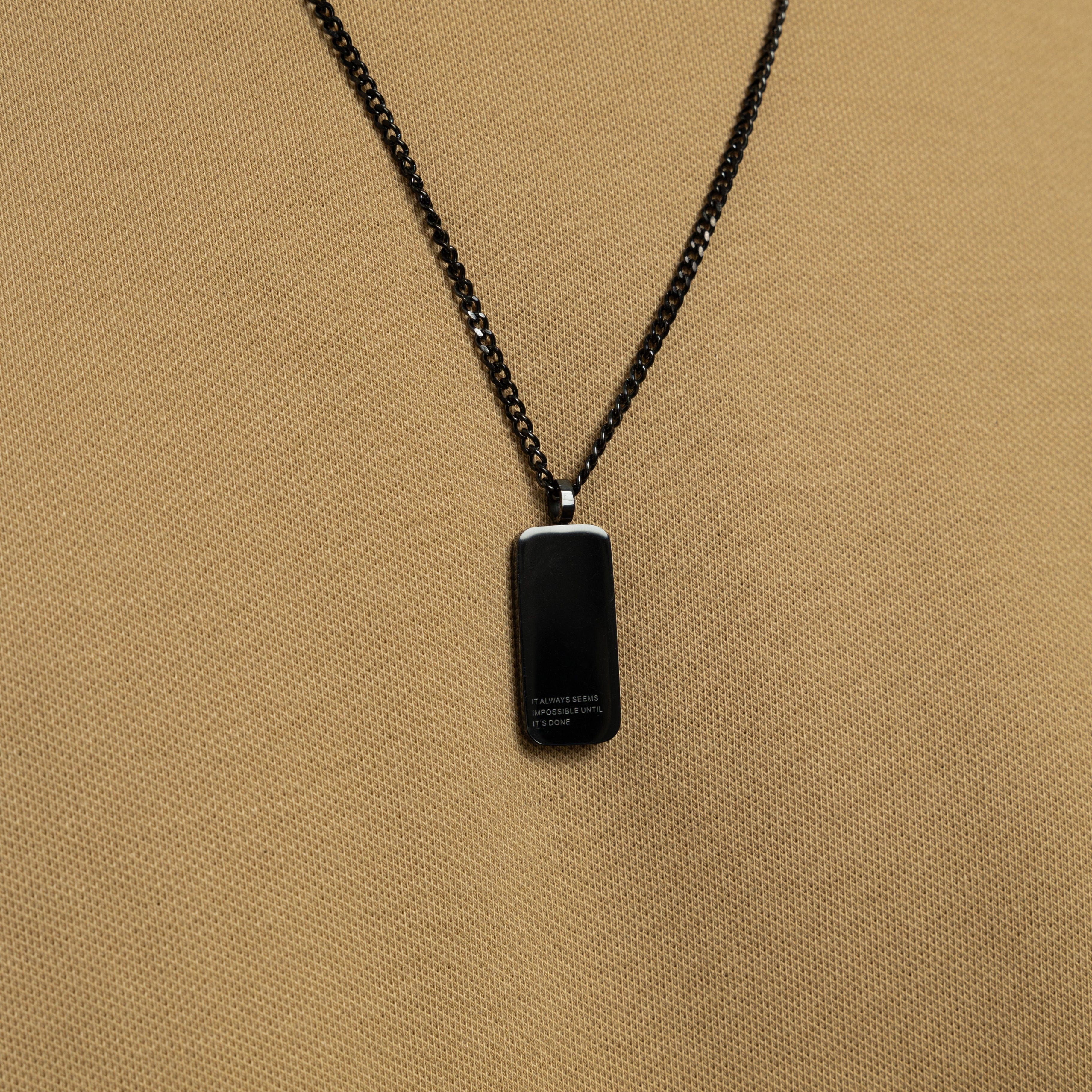 Close-up of stainless steel tag necklace resting on black velvet pouch