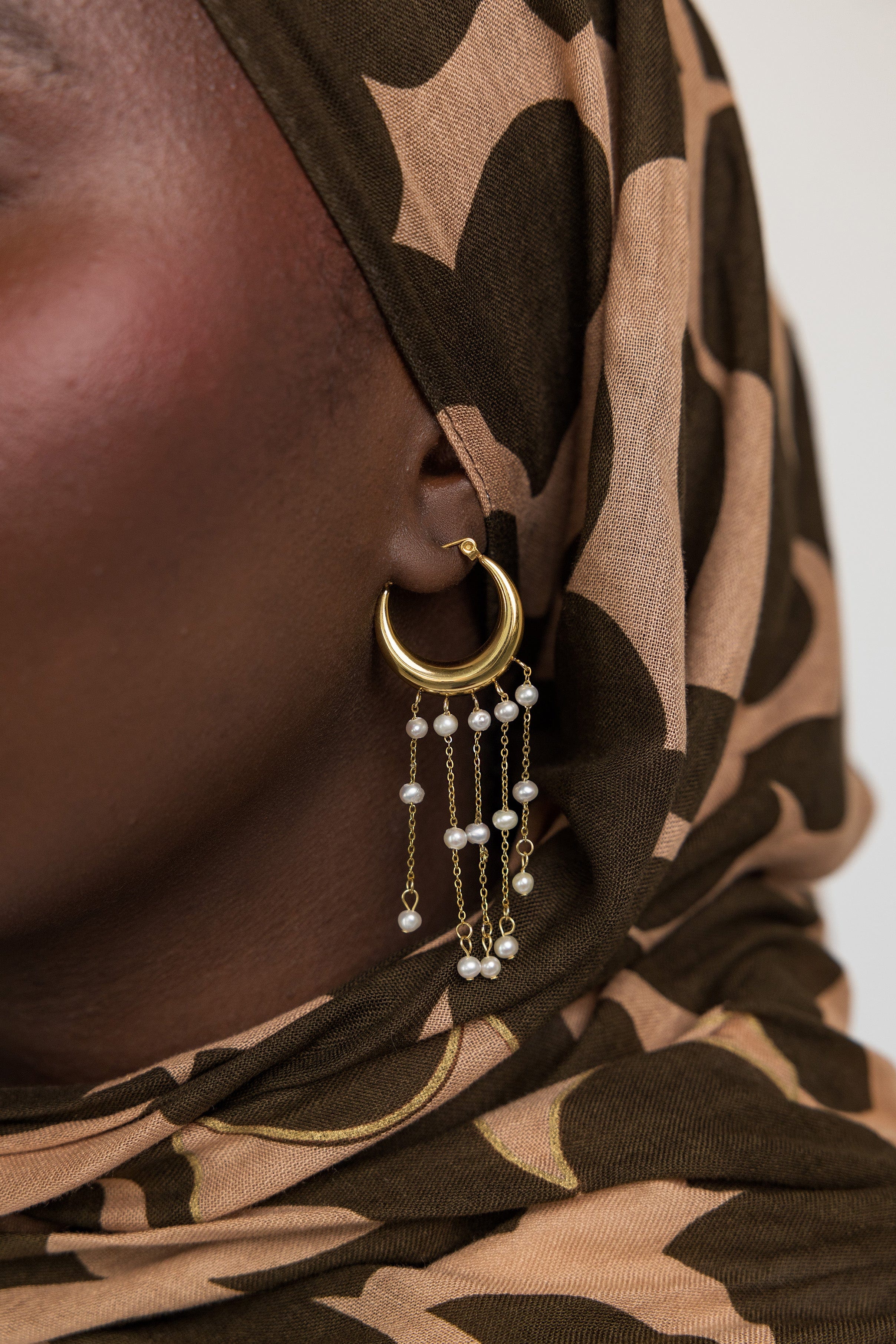 Model wearing gold hoop earrings with pearls, highlighting their elegance in a casual setting.