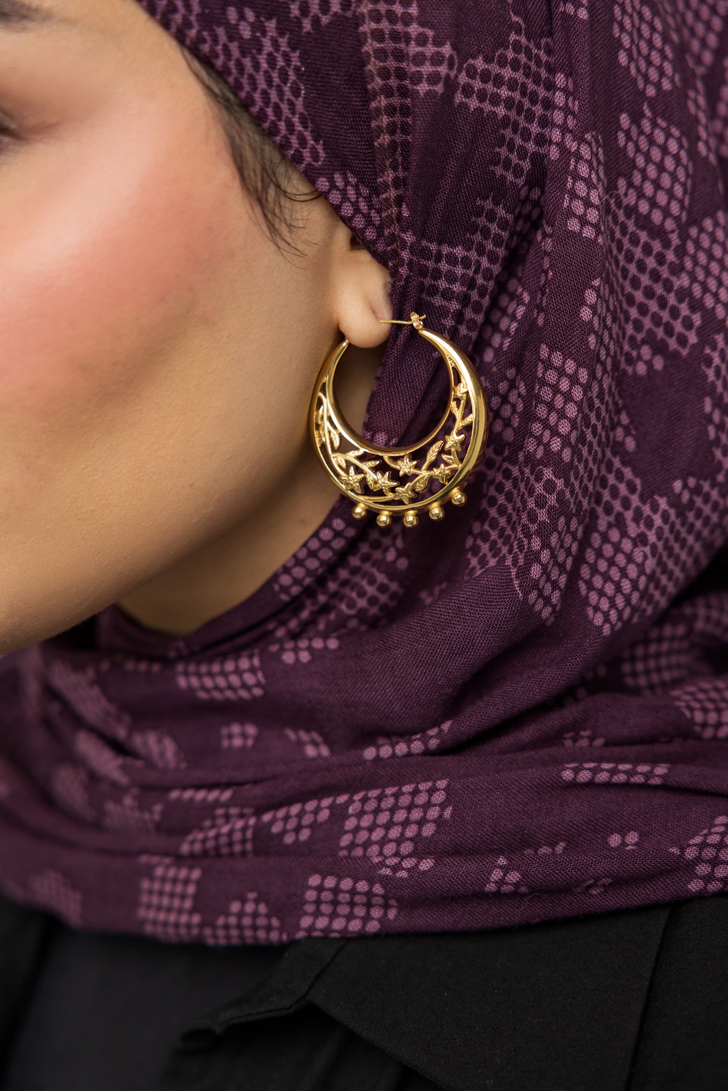 Close-up of jasmine crescent hoop earrings highlighting botanical details.