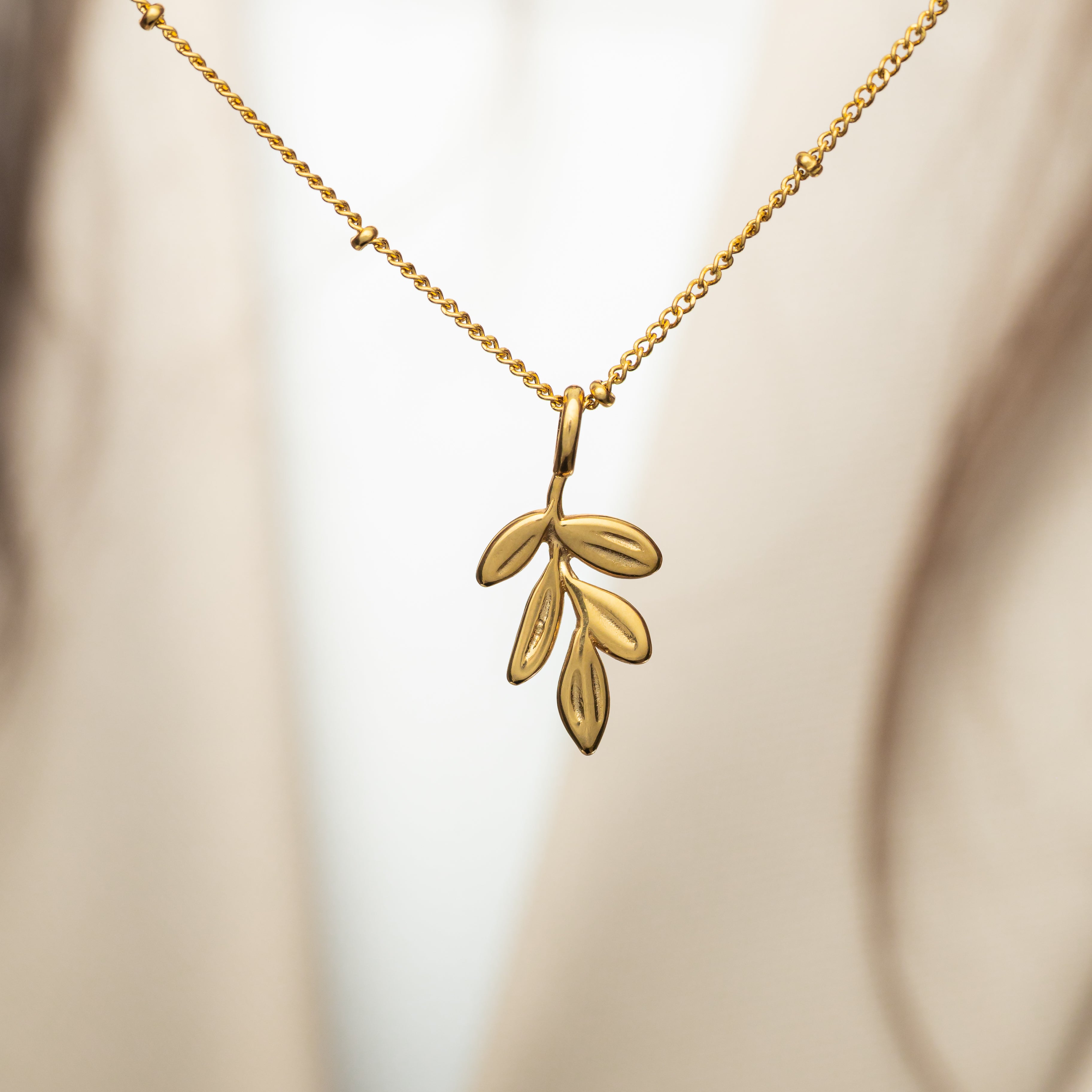 Olive branch charm displayed on a necklace, showcasing its elegance and symbolism.