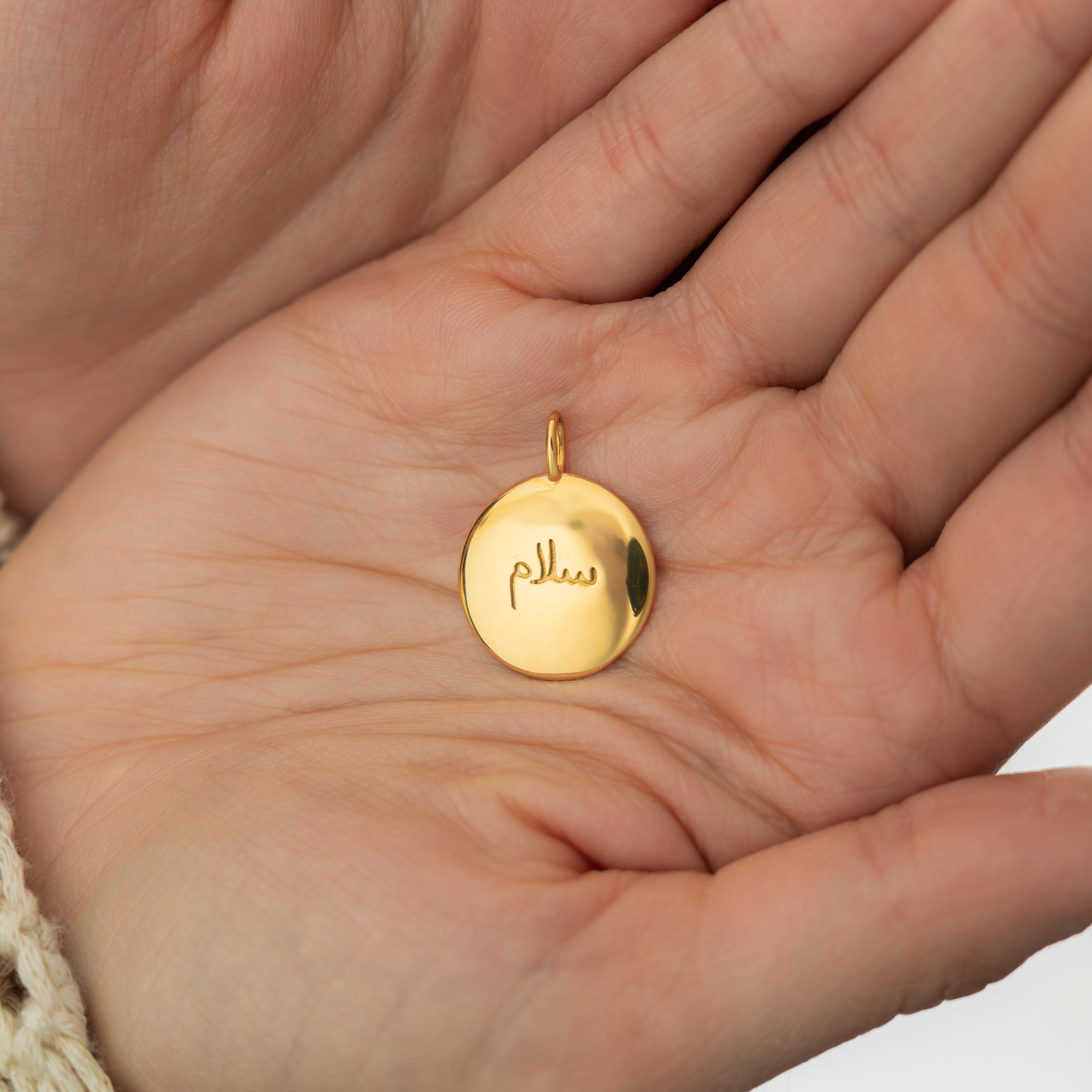 Gold charm stacked with other elegant jewelry pieces.