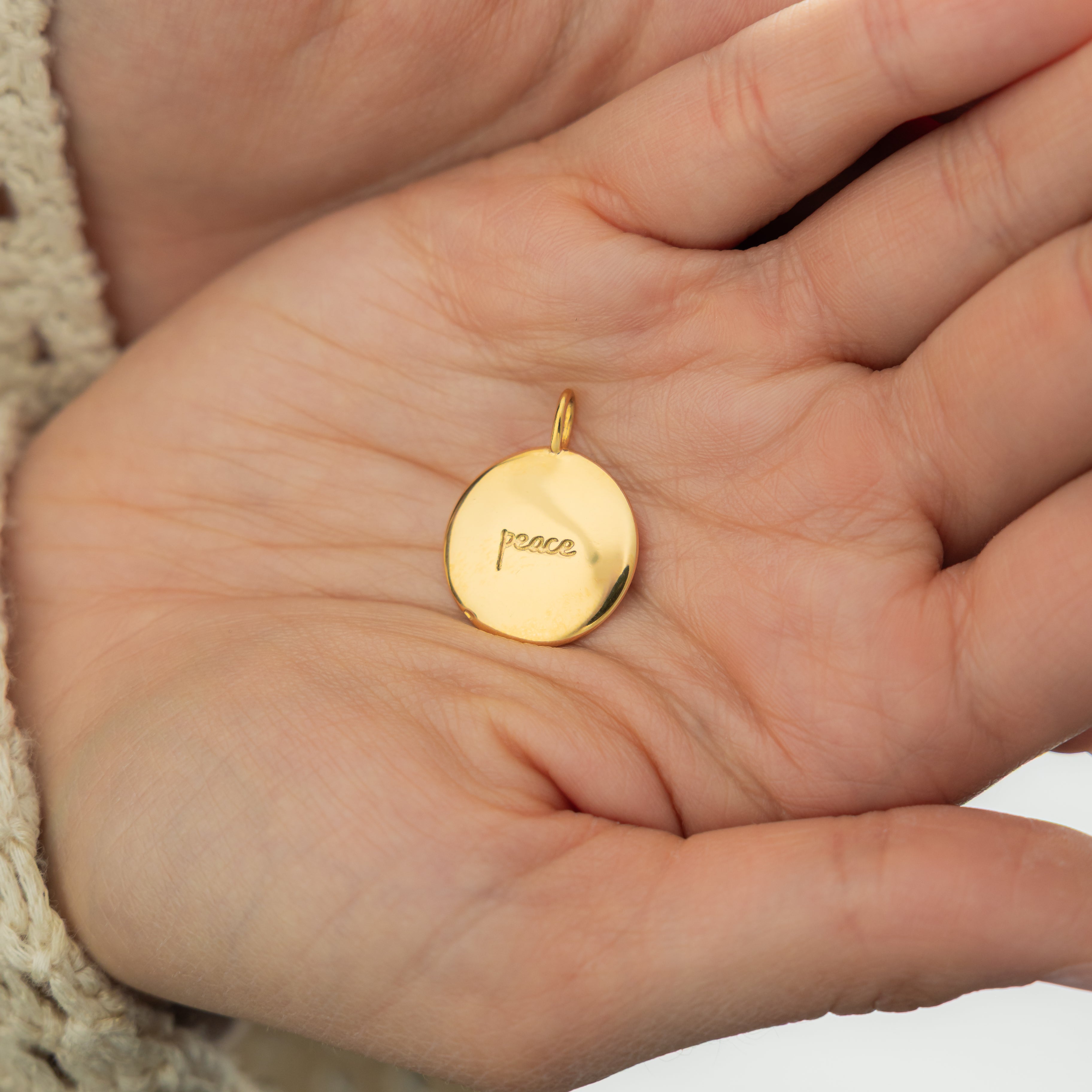 Gold charm stacked with other elegant jewelry pieces.