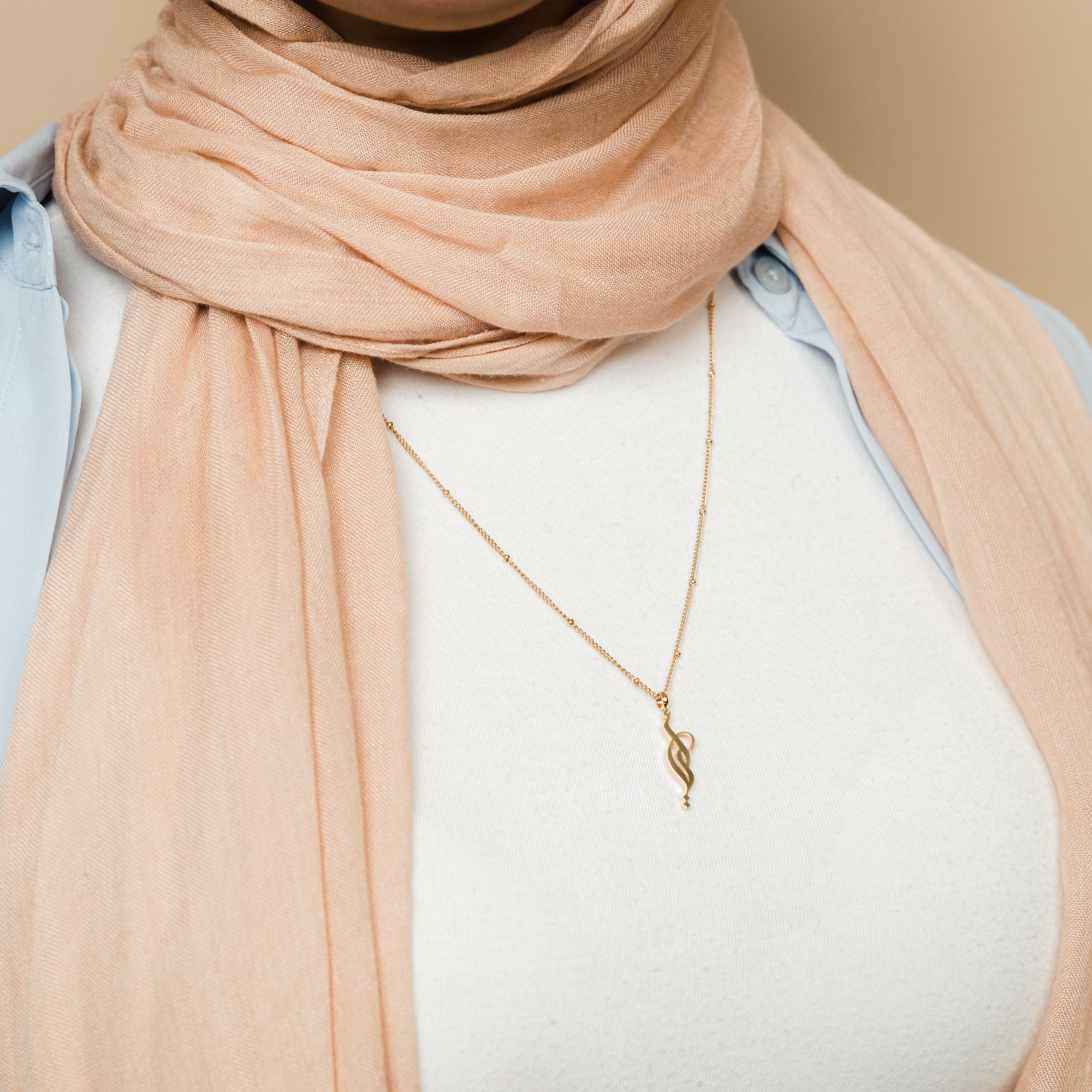 Mother wearing the gold plated necklace with Arabic script while holding child