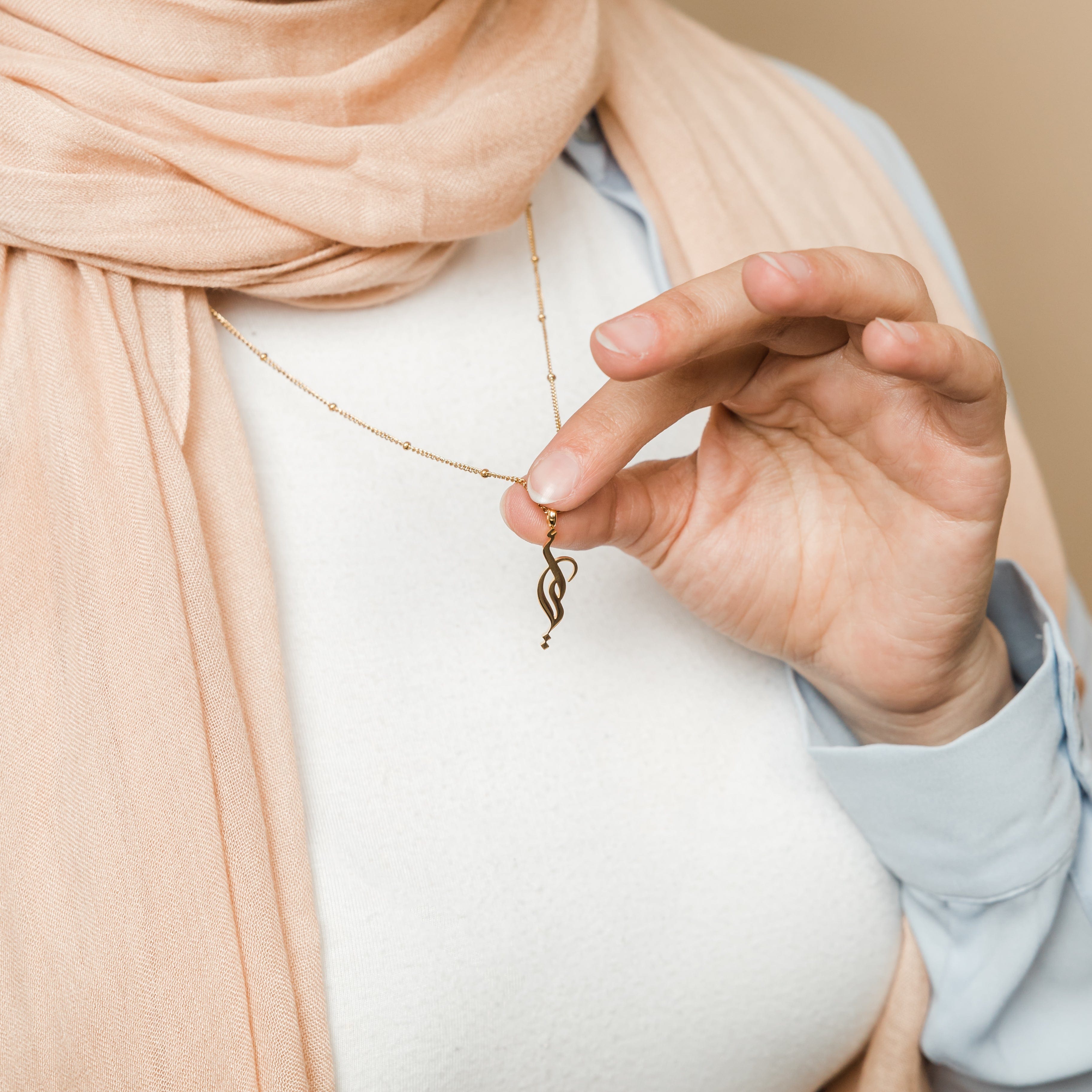 Mother wearing the gold plated necklace with Arabic script while holding child