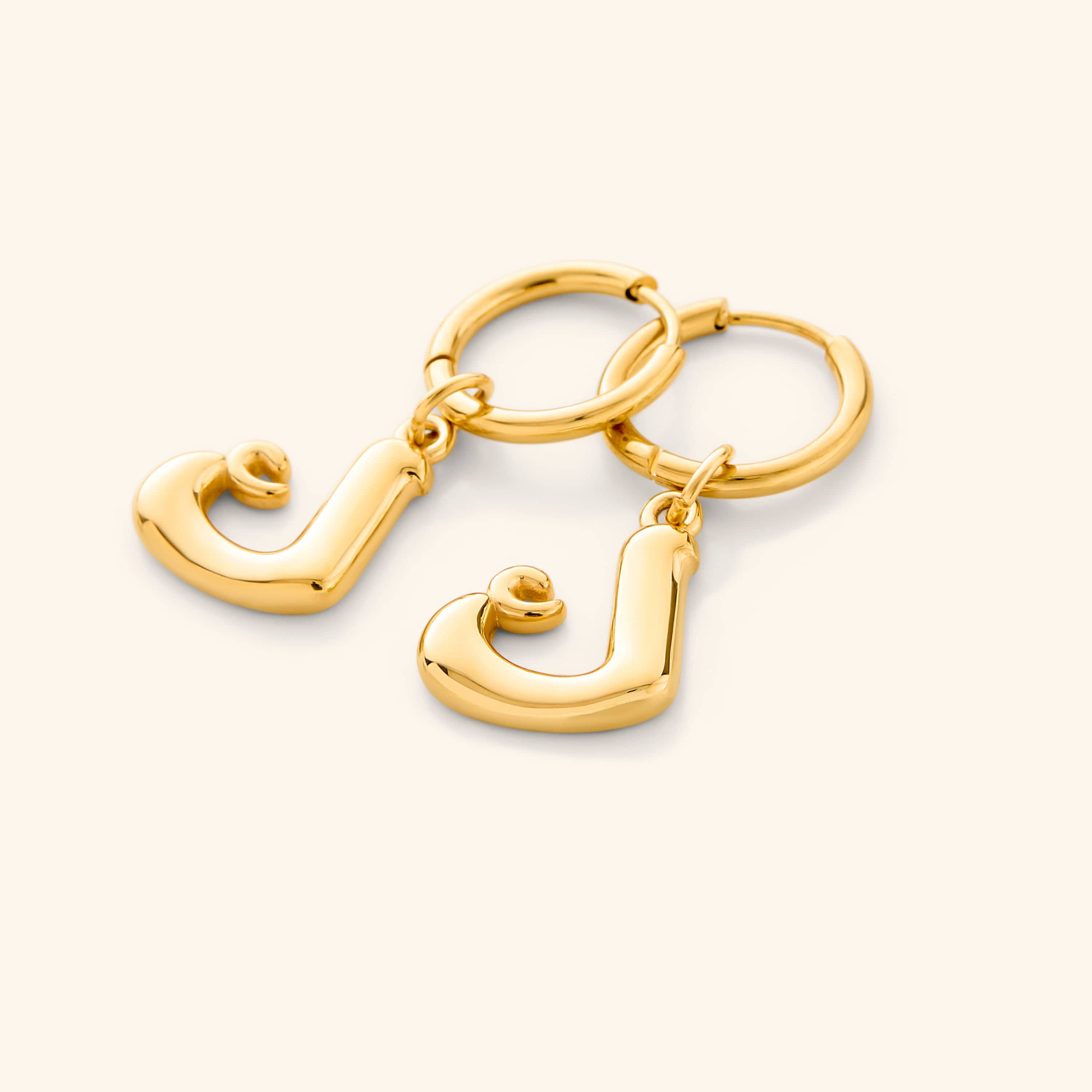 Close-up of gold bubble letter earrings featuring Arabic initials, shown against velvet pouch
