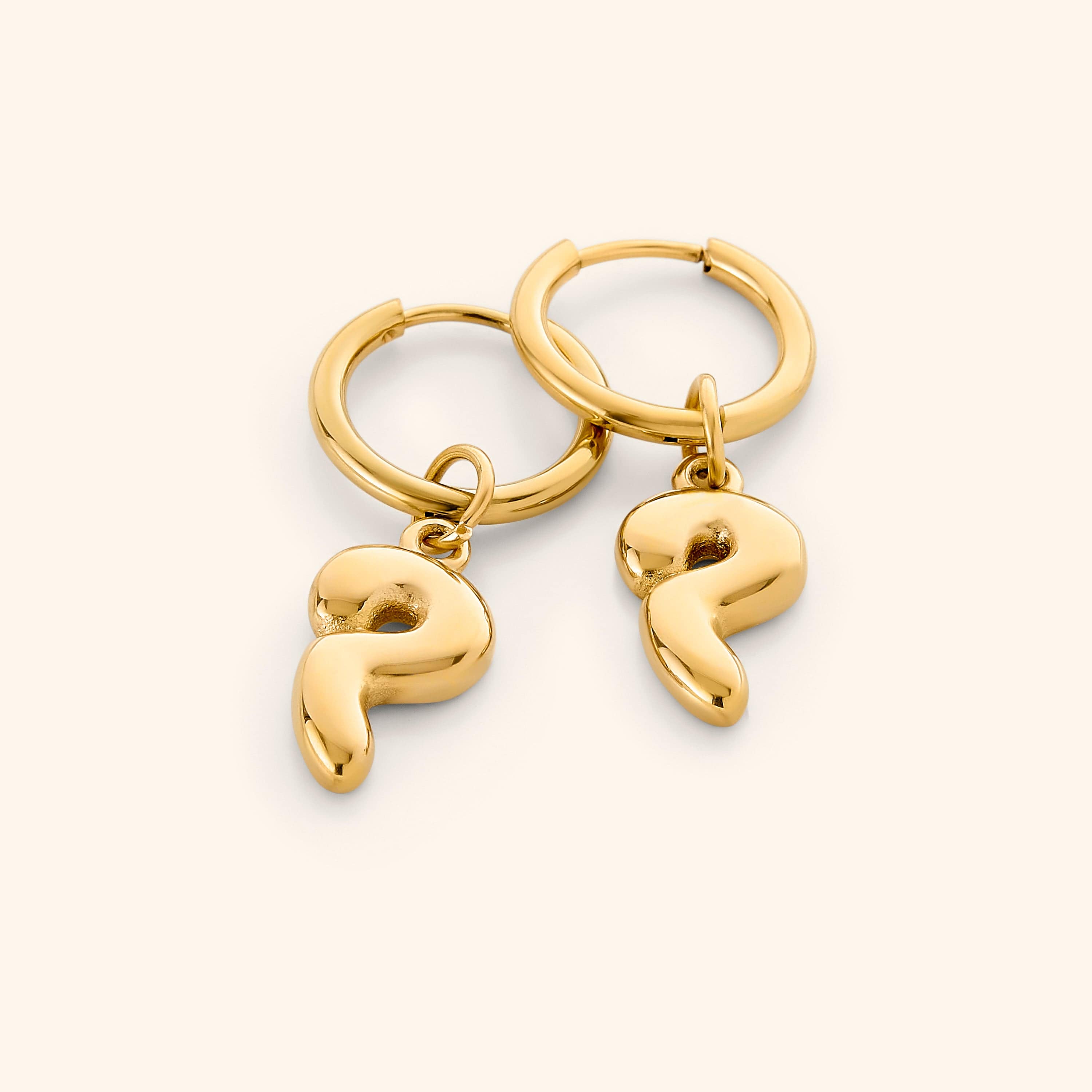 Close-up of gold bubble letter earrings featuring Arabic initials, shown against velvet pouch
