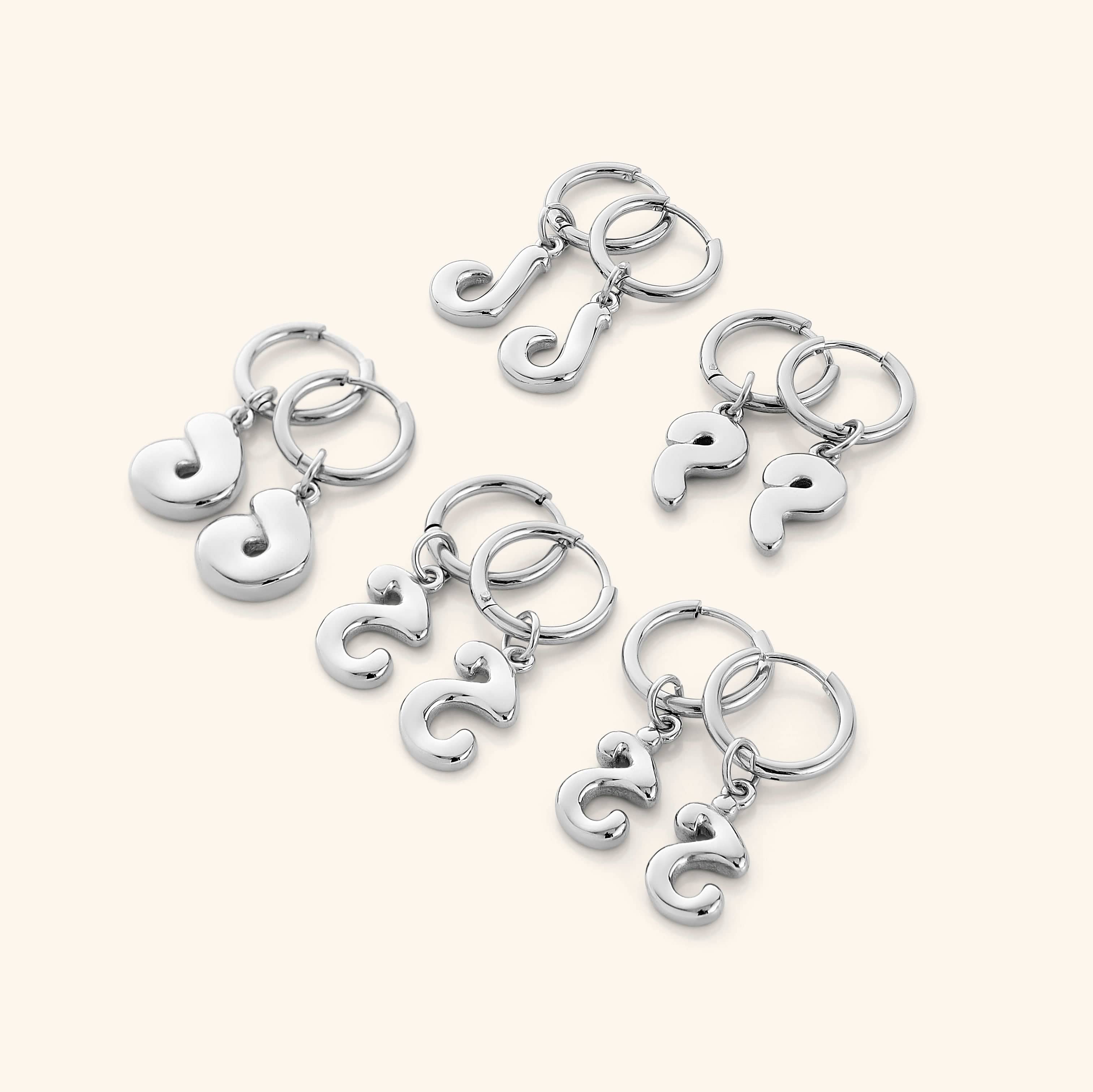 Flatlay of the earrings with packaging, showcasing trendy initial design and gold finish