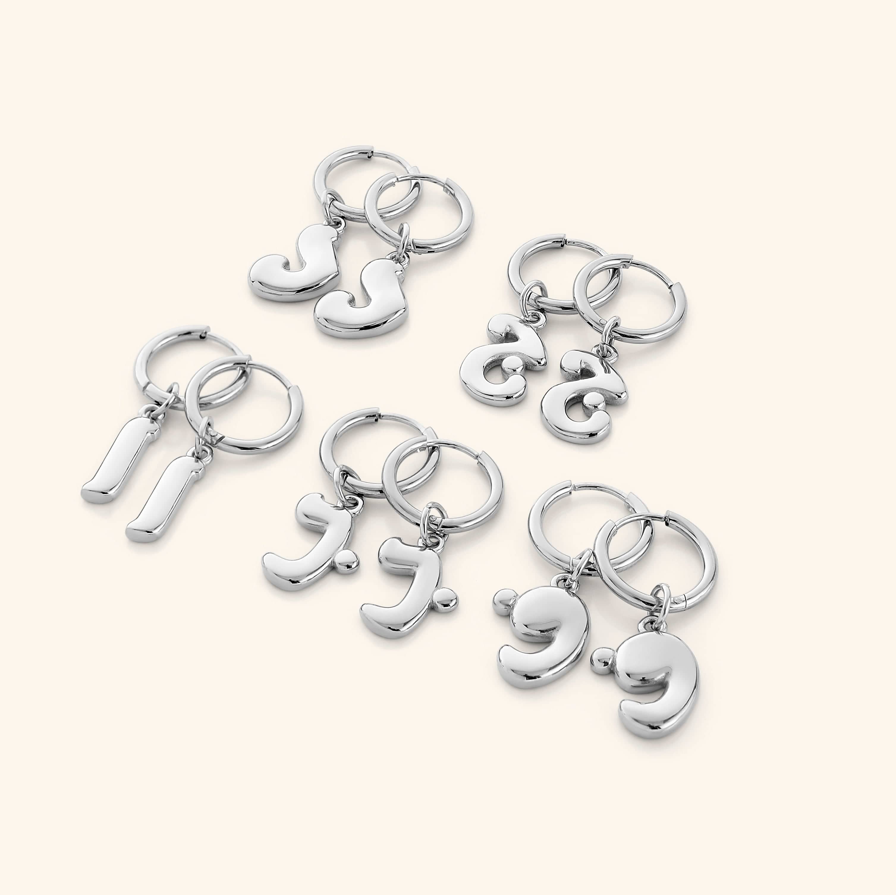Close-up of gold bubble letter earrings featuring Arabic initials, shown against velvet pouch