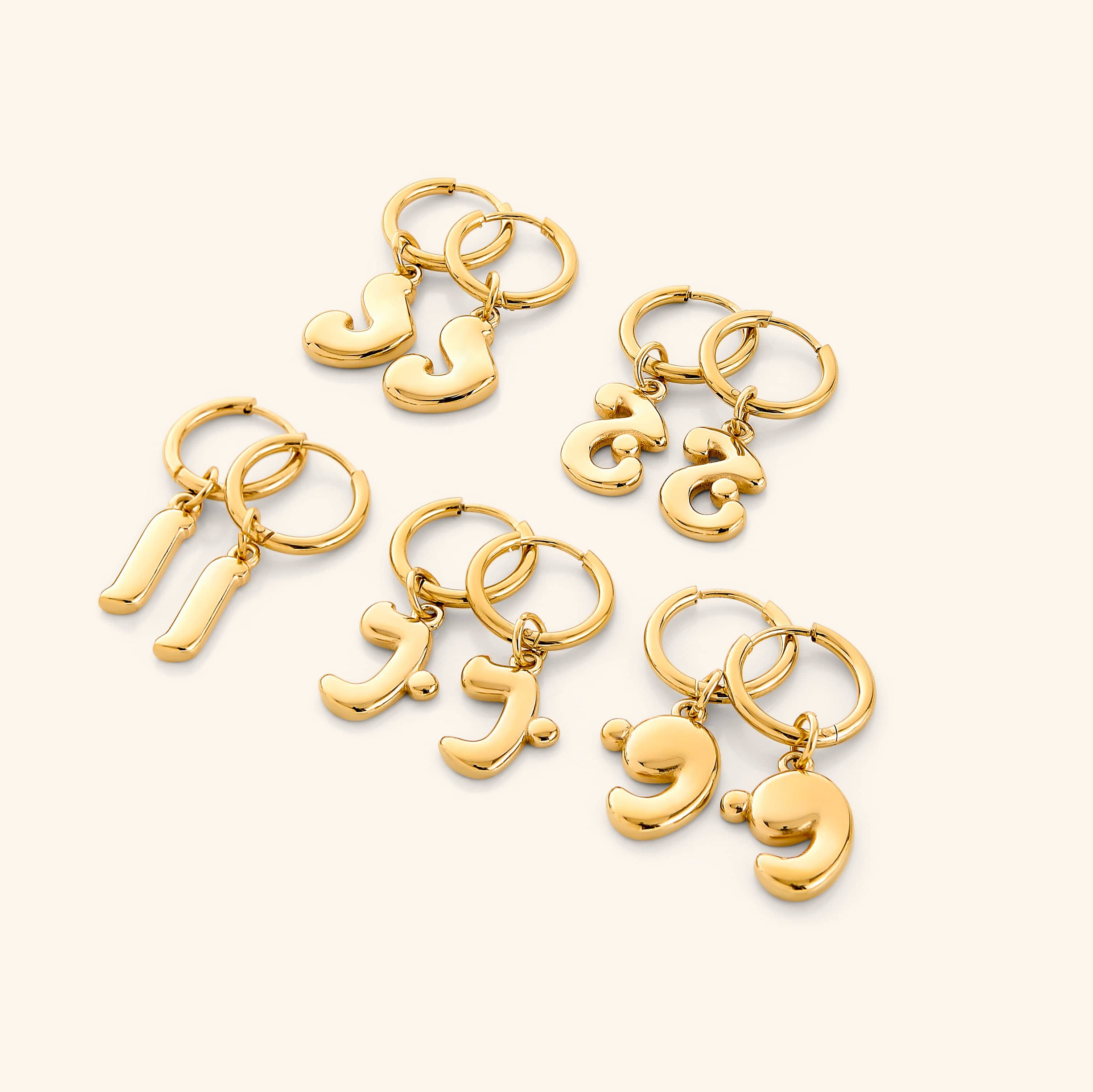 Close-up of gold bubble letter earrings featuring Arabic initials, shown against velvet pouch