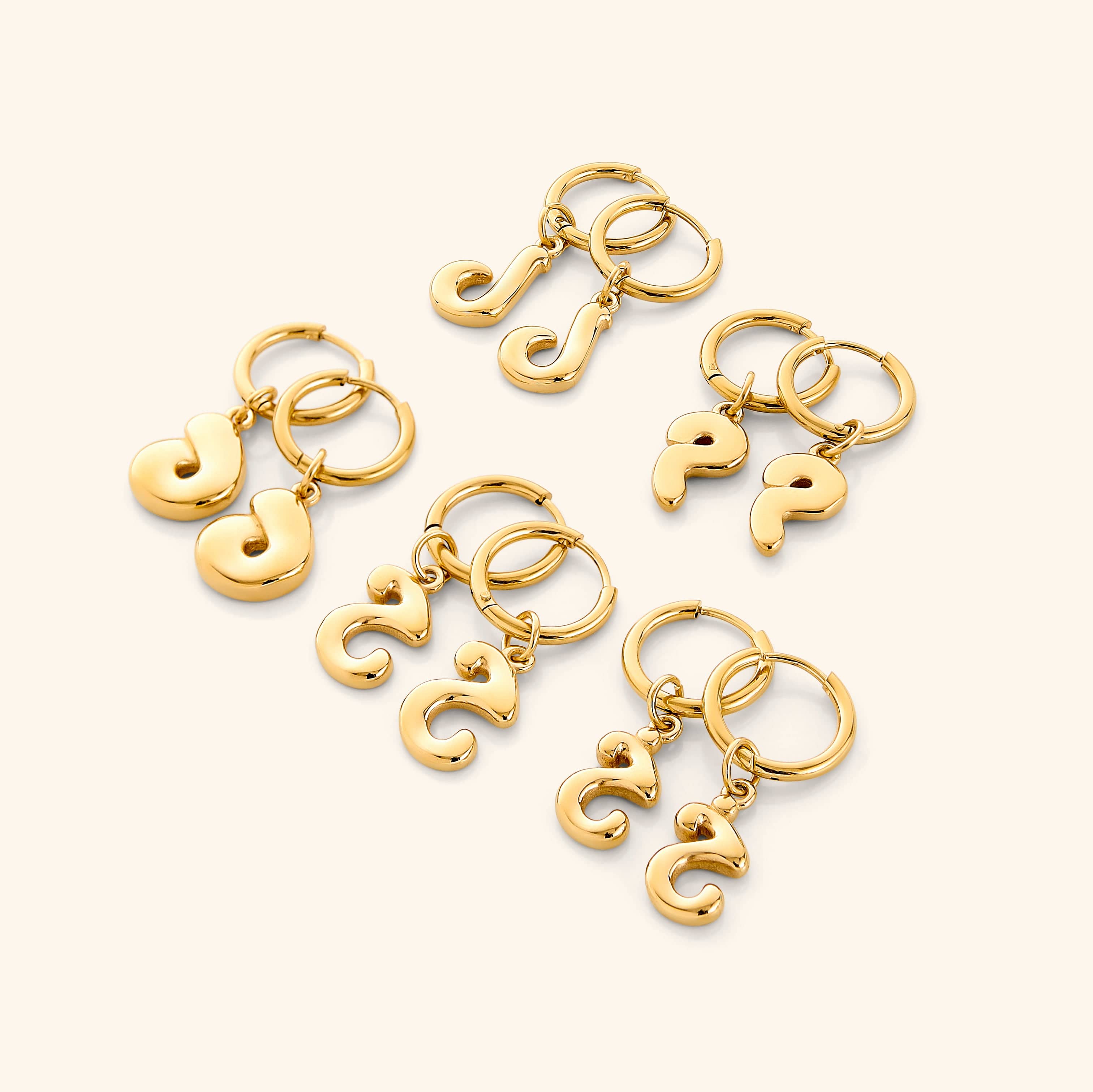 Flatlay of the earrings with packaging, showcasing trendy initial design and gold finish