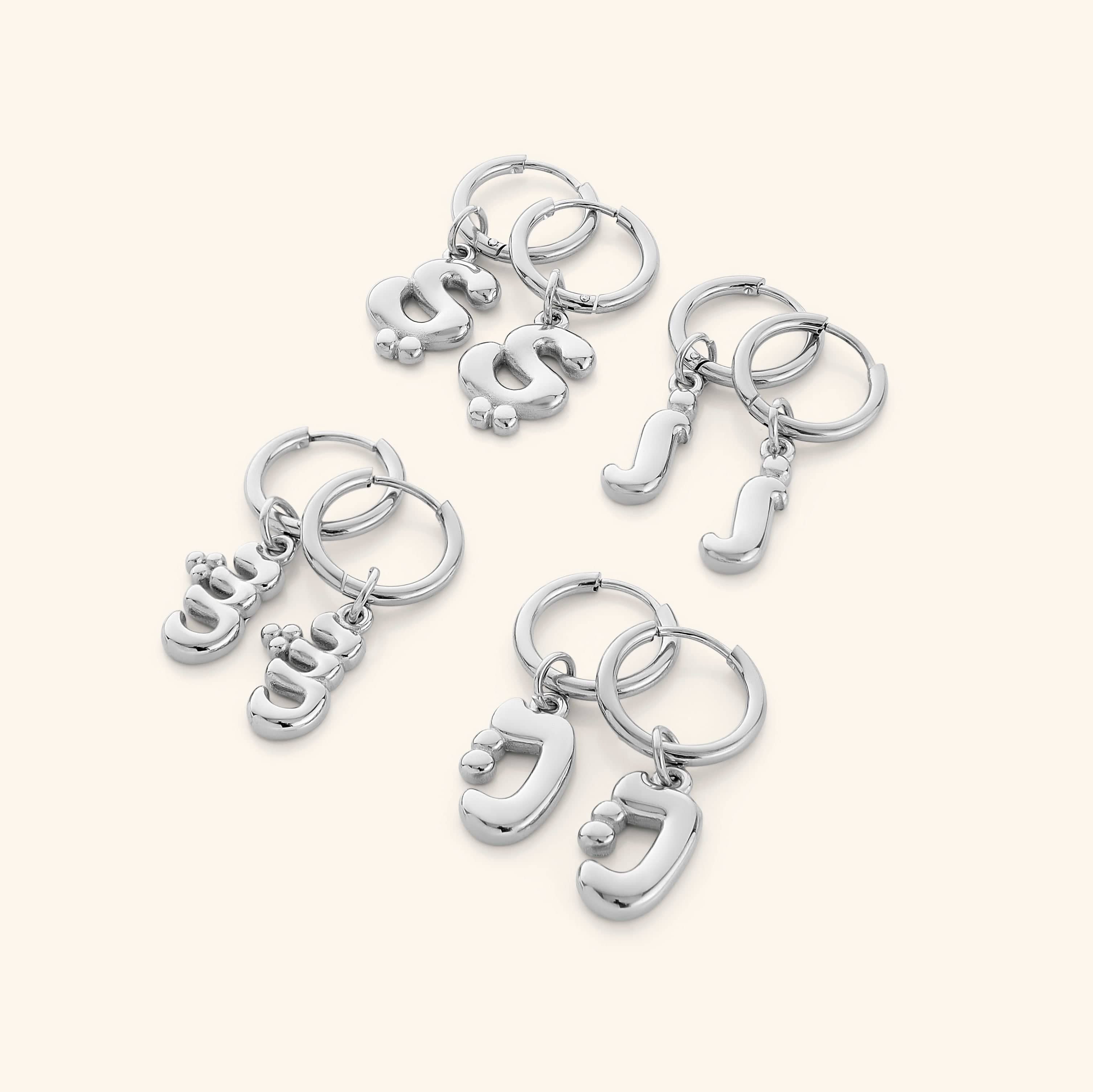 Flatlay of the earrings with packaging, showcasing trendy initial design and gold finish