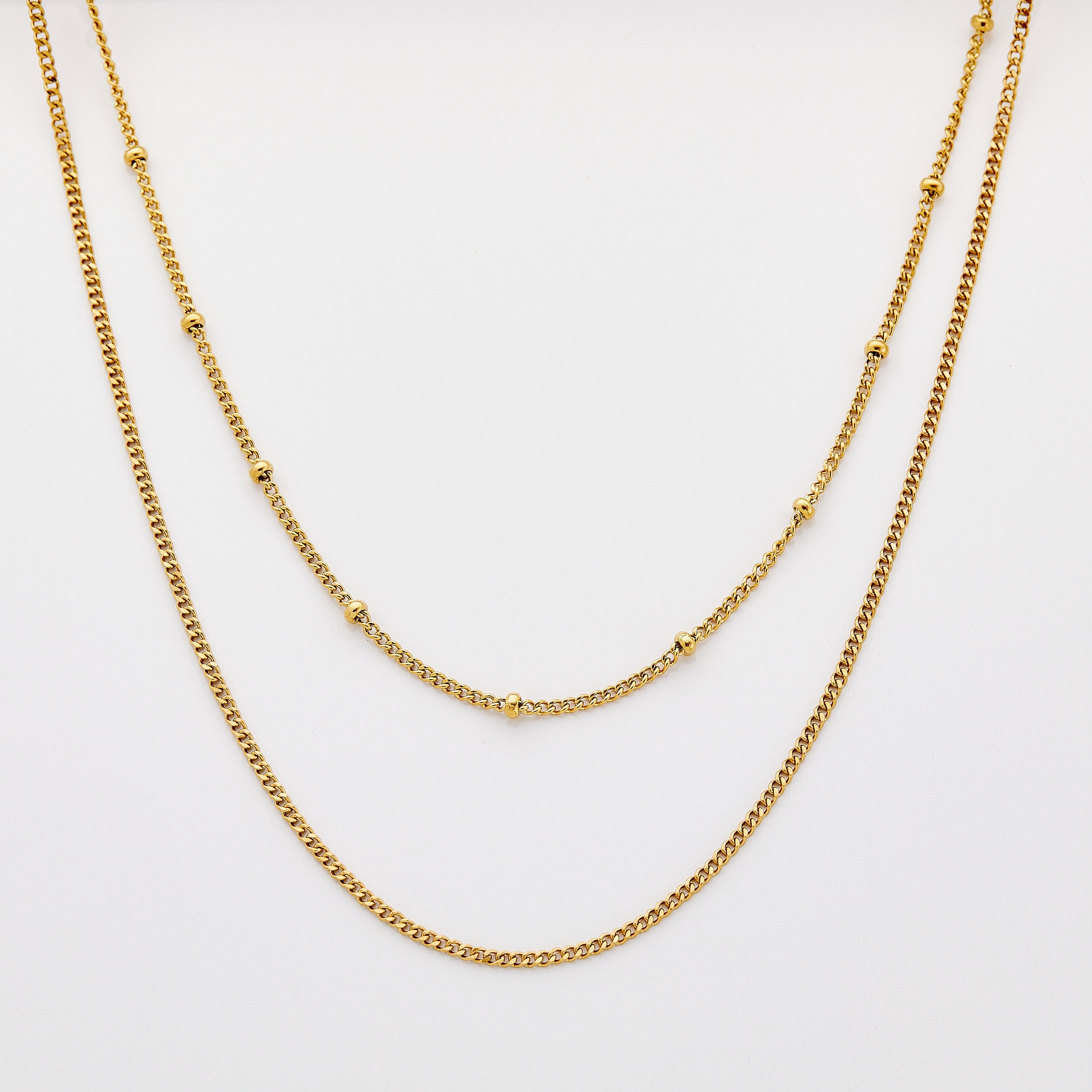 Close-up of Cuban and dotted gold chains layered at mid-length for a sleek look