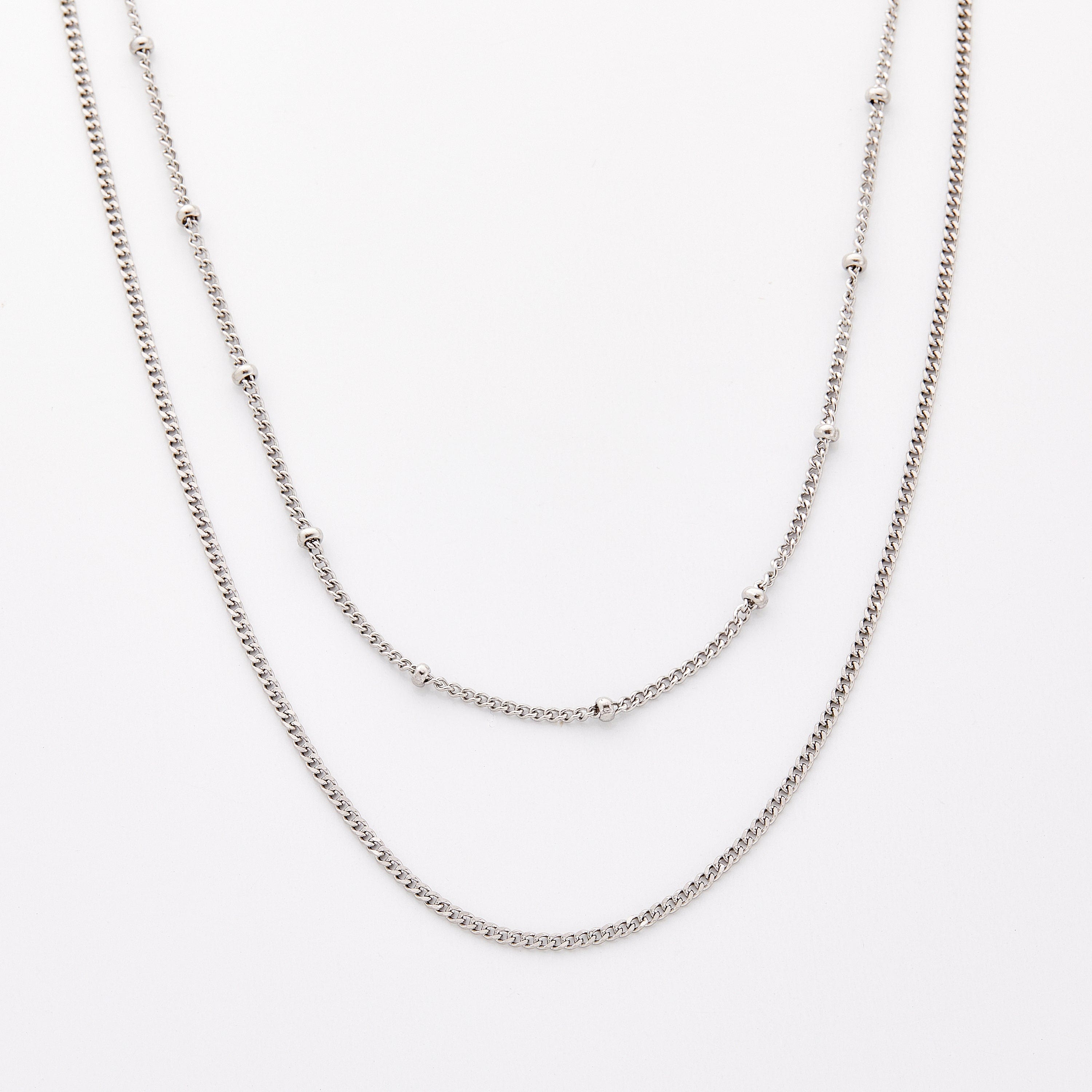 Close-up of Cuban and dotted gold chains layered at mid-length for a sleek look