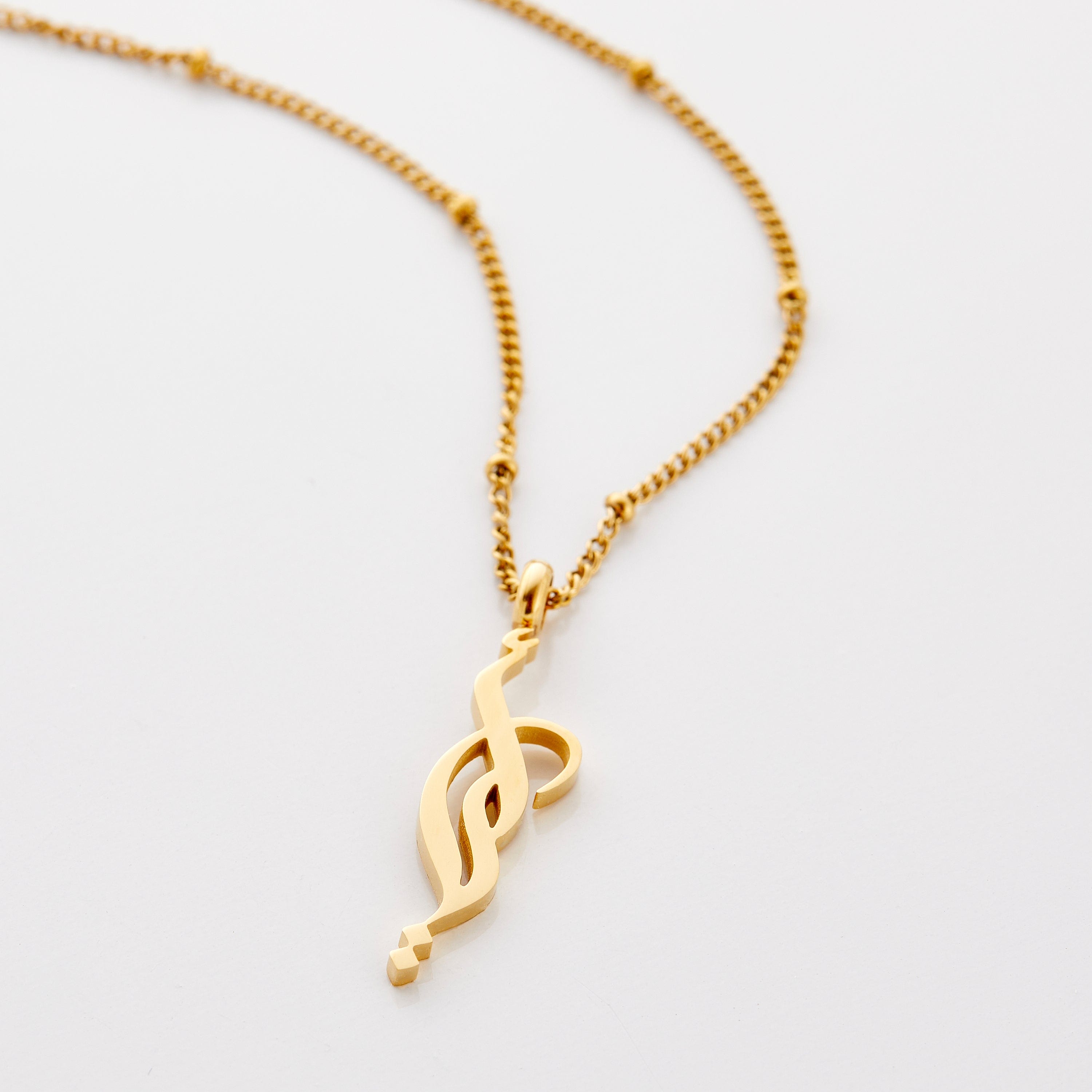 Close-up of the cradle-style Arabic calligraphy necklace resting on silk fabric