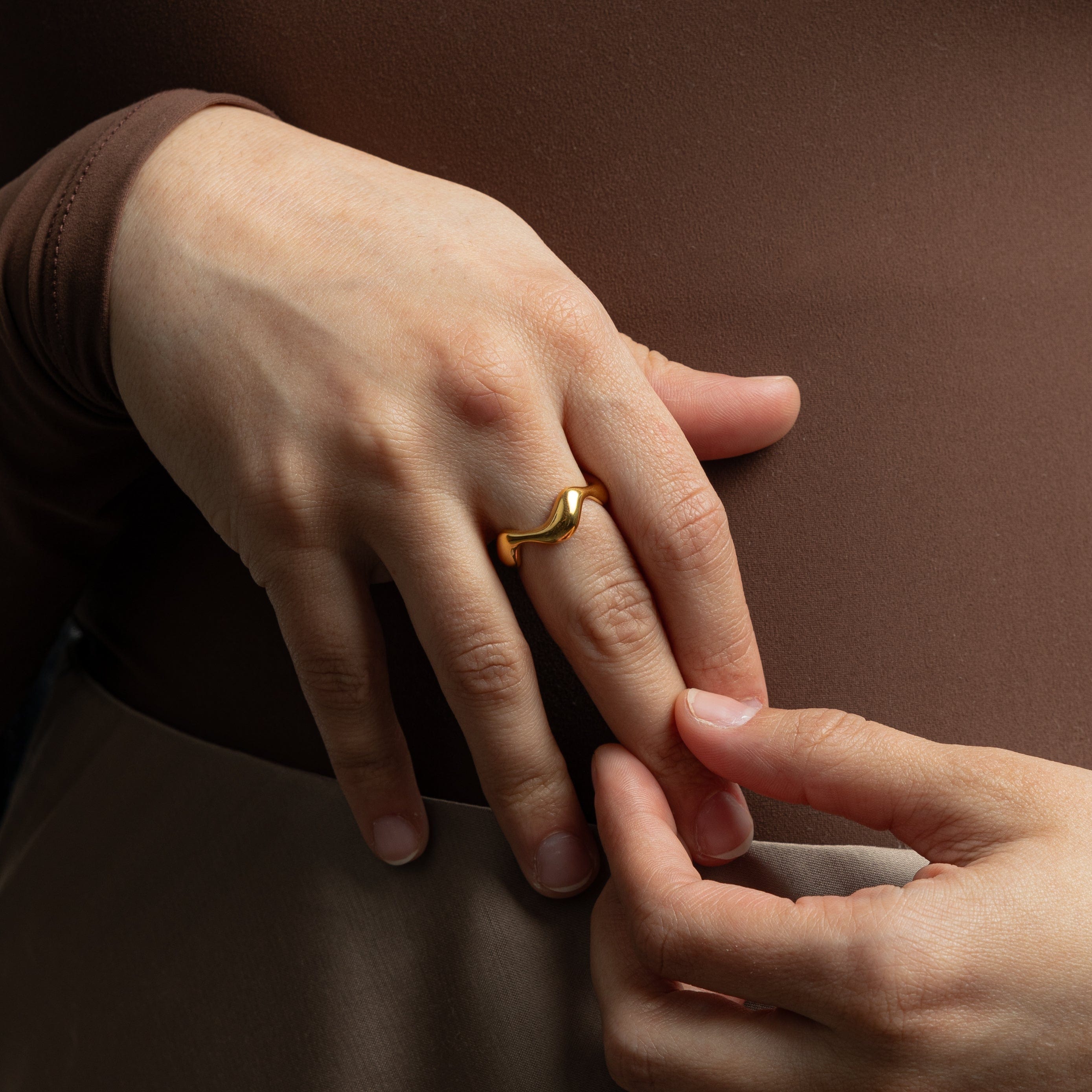 Oceanic Wave Gold Ring on a beach background, symbolizing its ocean-inspired theme.