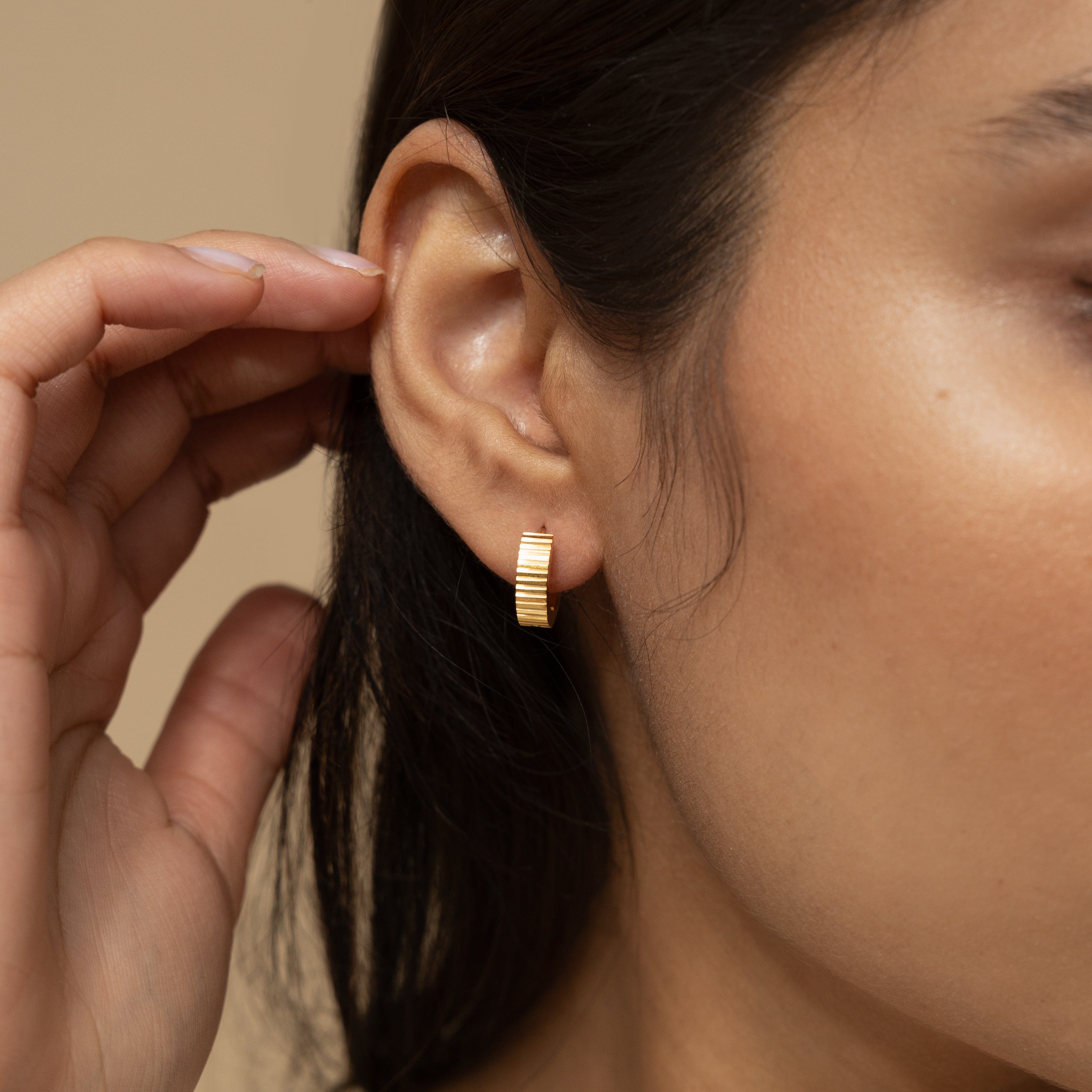 Close-up of small gold hoops with ridged design, highlighting quality craftsmanship.