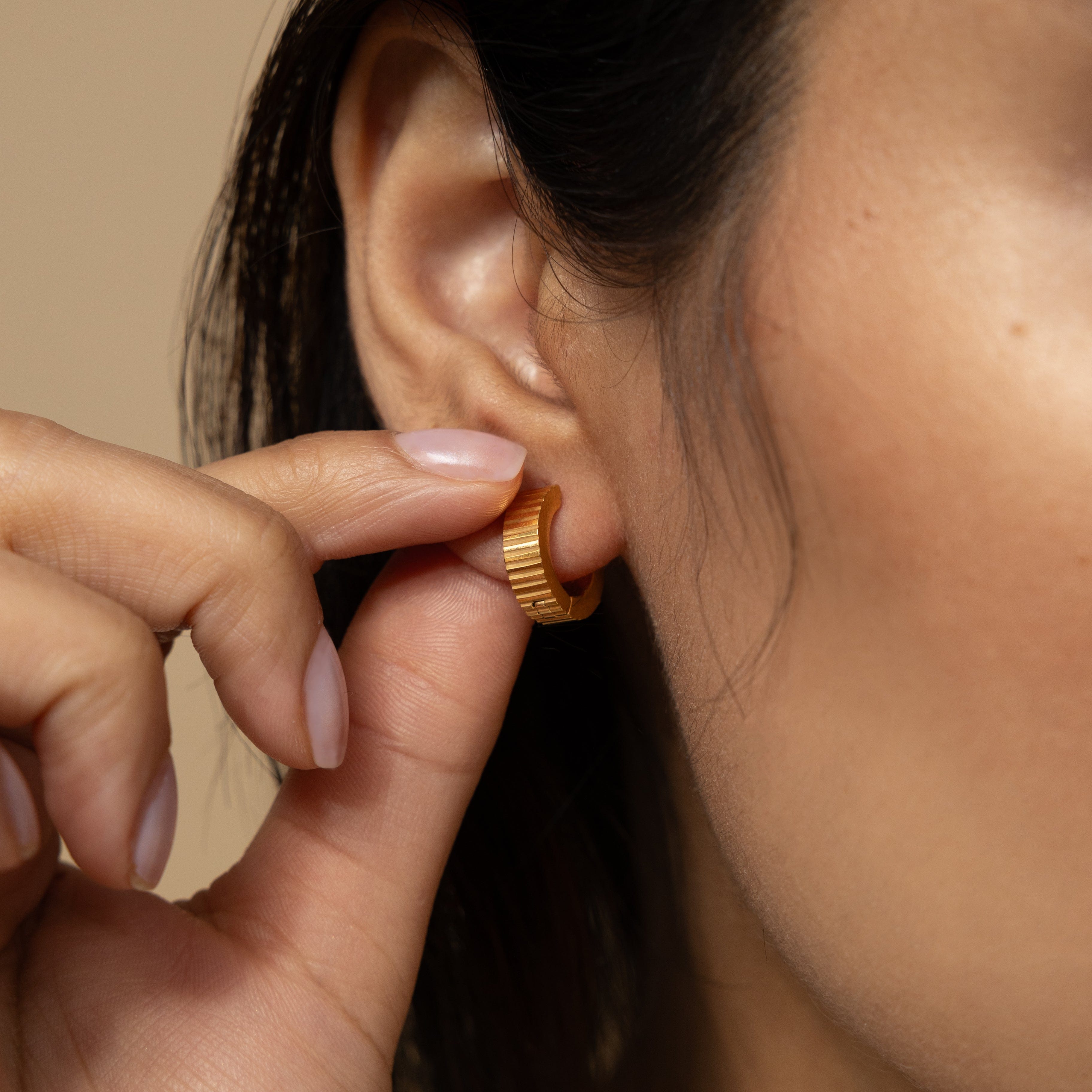 Close-up of small gold hoops with ridged design, highlighting quality craftsmanship.