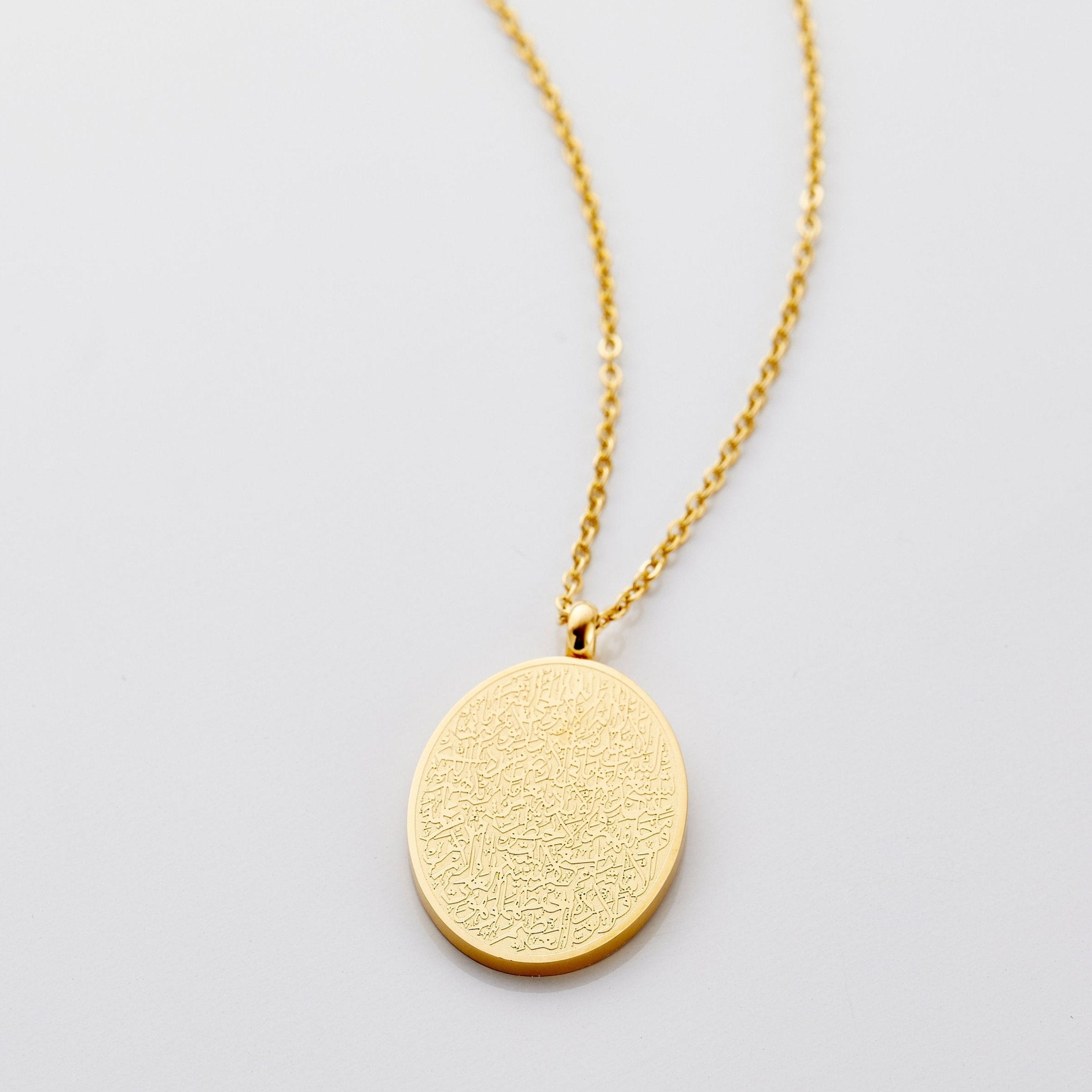 Elegant Ayatul Kursi gold pendant necklace displayed on a velvet pouch, showcasing its intricate engraving and design.