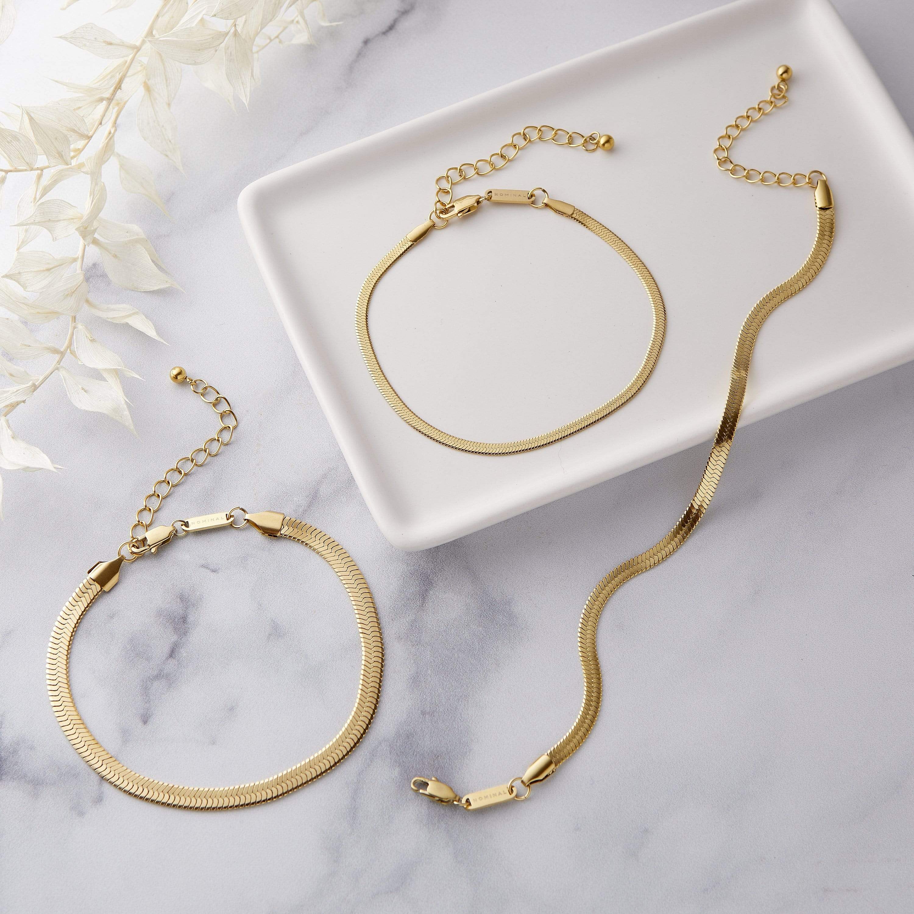 Elegant herringbone chain anklet displayed on a wooden surface, showcasing its shine and intricate design.