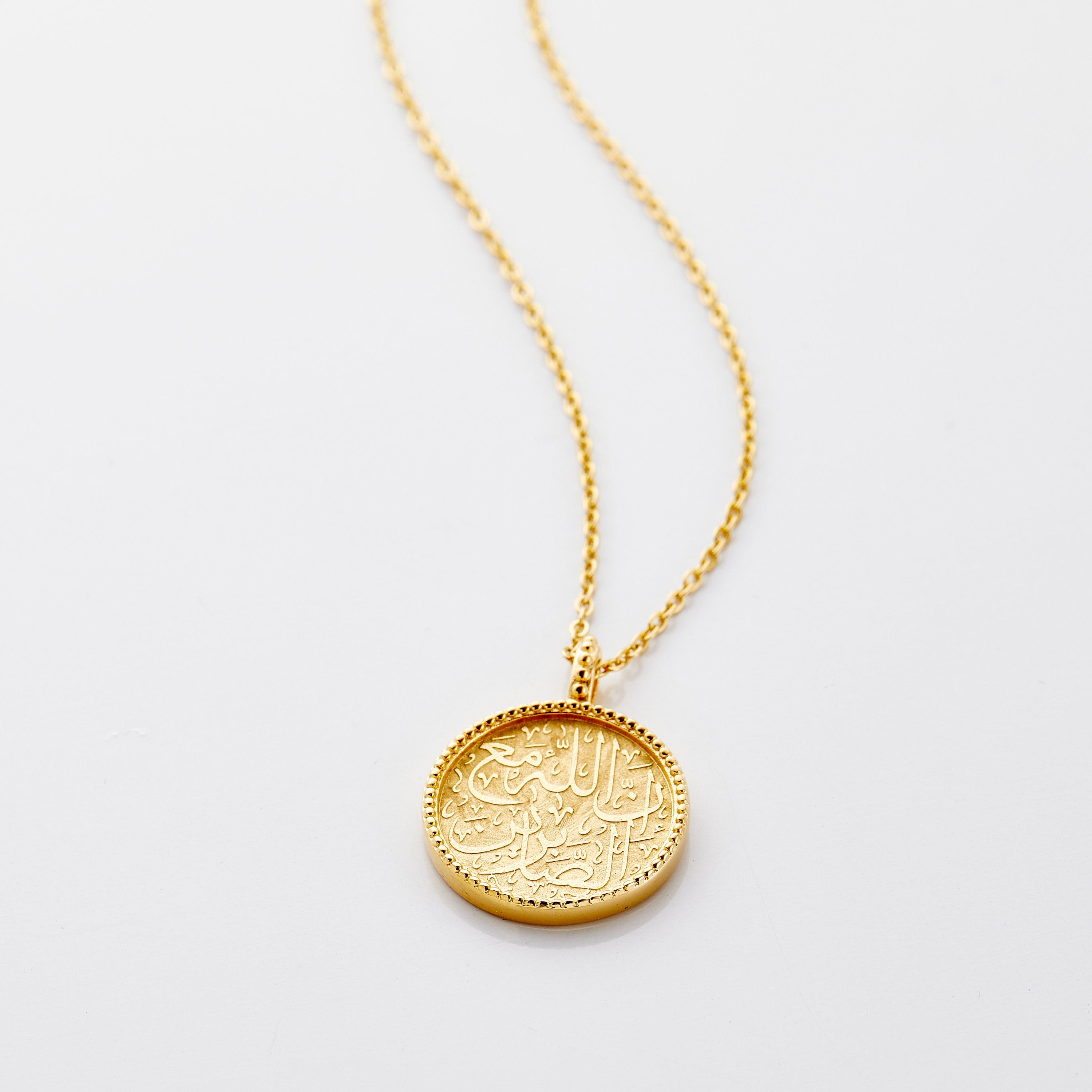 Close-up of the religious pendant showing Quran verse engraving with vintage ridged edges